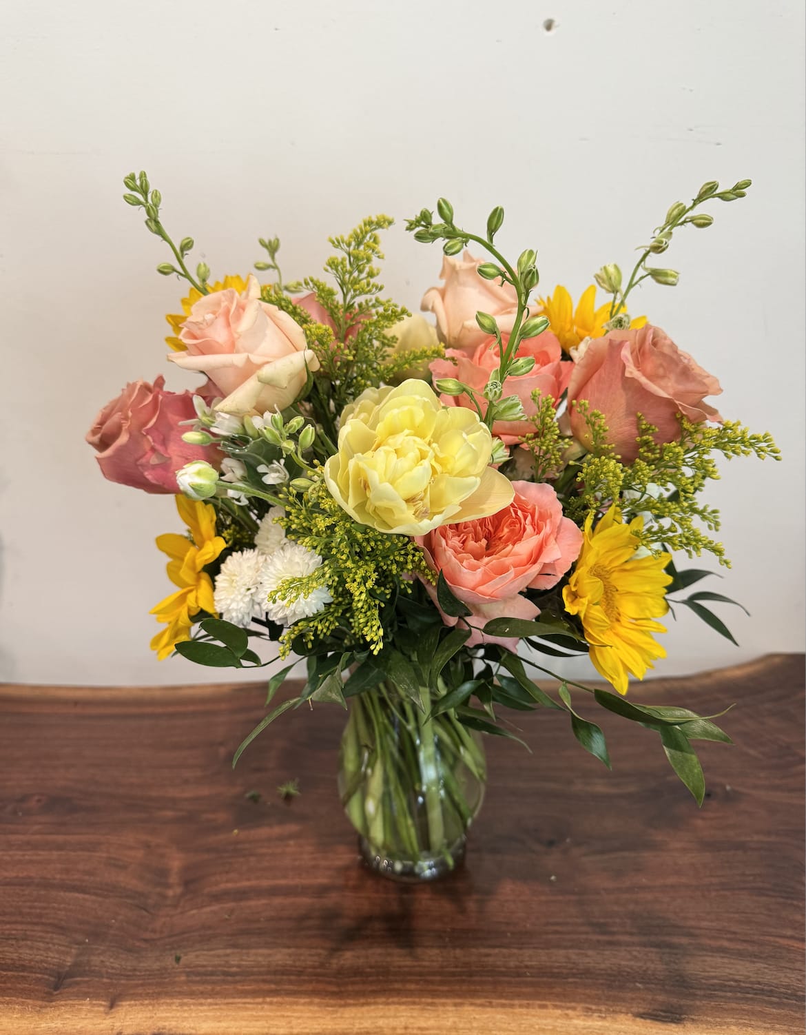 Li'l Miss Sunshine - Peach and coral roses meet bold yellow sunflowers and seasonal stems in a bright, cheerful mixed bouquet perfect as a birthday bouquet, thank-you gift, or spring celebration arrangement. Li'l Miss Sunshine reads warm and uplifting-she'll feel both adored and energized by the sunny yellow tones balanced with soft pinks and crisp white accents.  