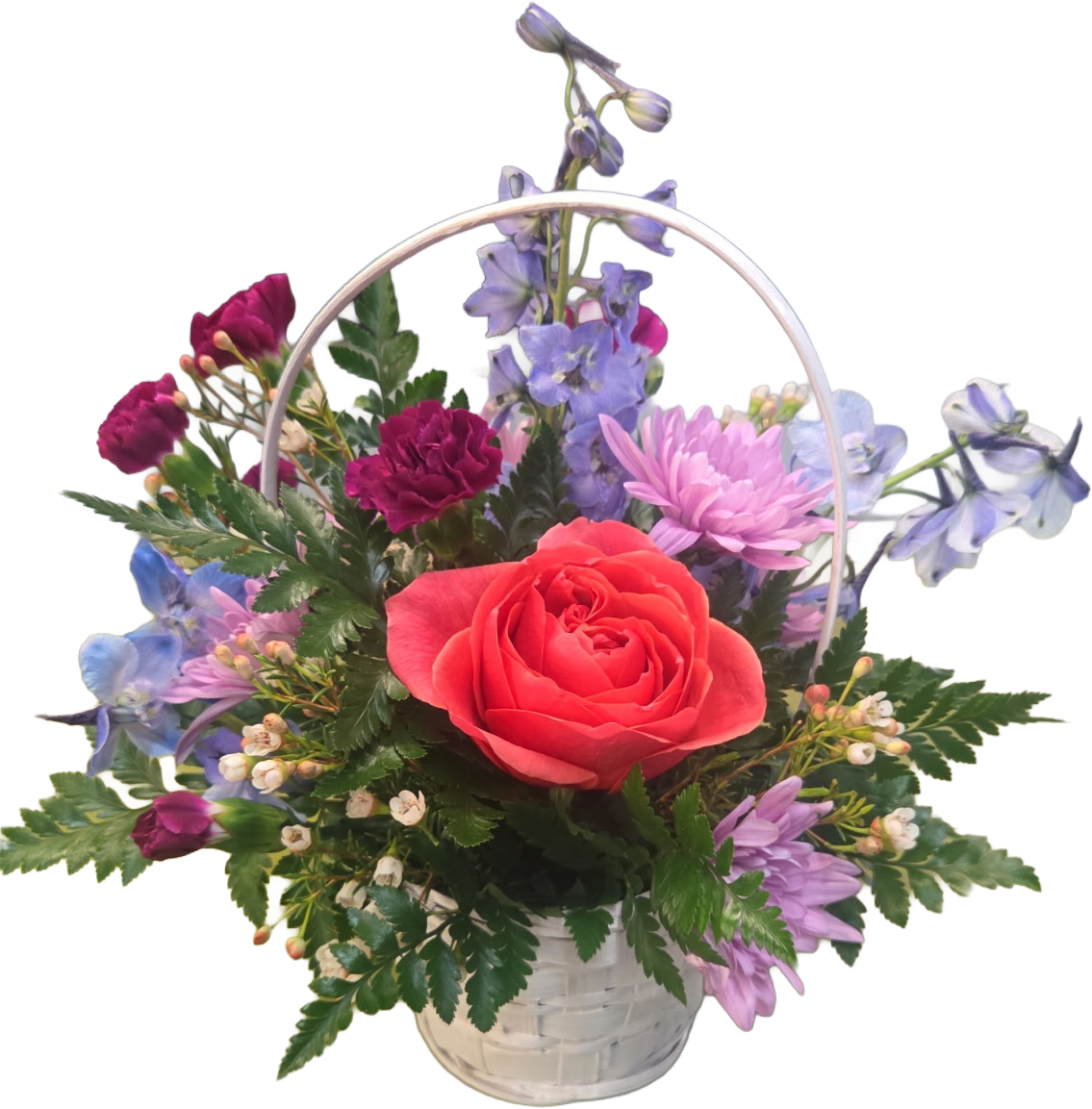 Bloom Basket - Soft pink and lavender chrysanthemum-like blooms and deep magenta carnations surround the focal rose, while airy blue-purple delphinium spikes add height and a delicate, breezy texture. Small white filler blossoms and layered green foliage fill the arrangement for a lush, full look that feels hand-gathered from a cottage garden.
