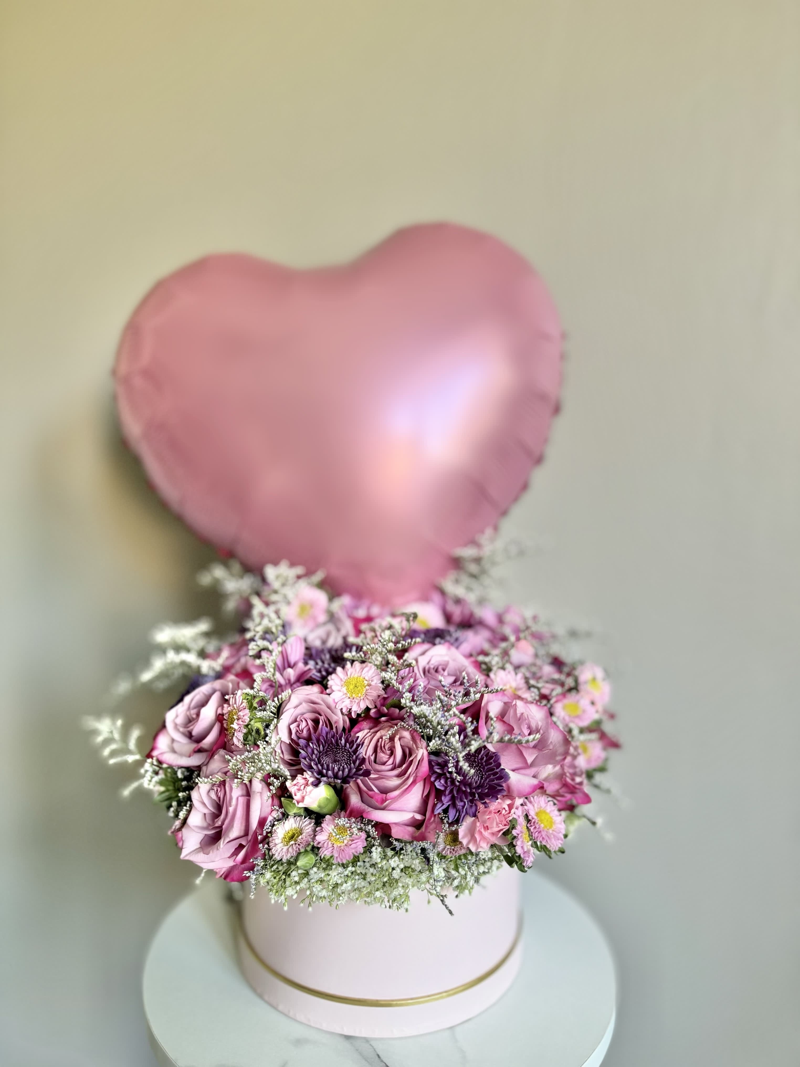 Pink heart balloon above a pink flower box arrangement