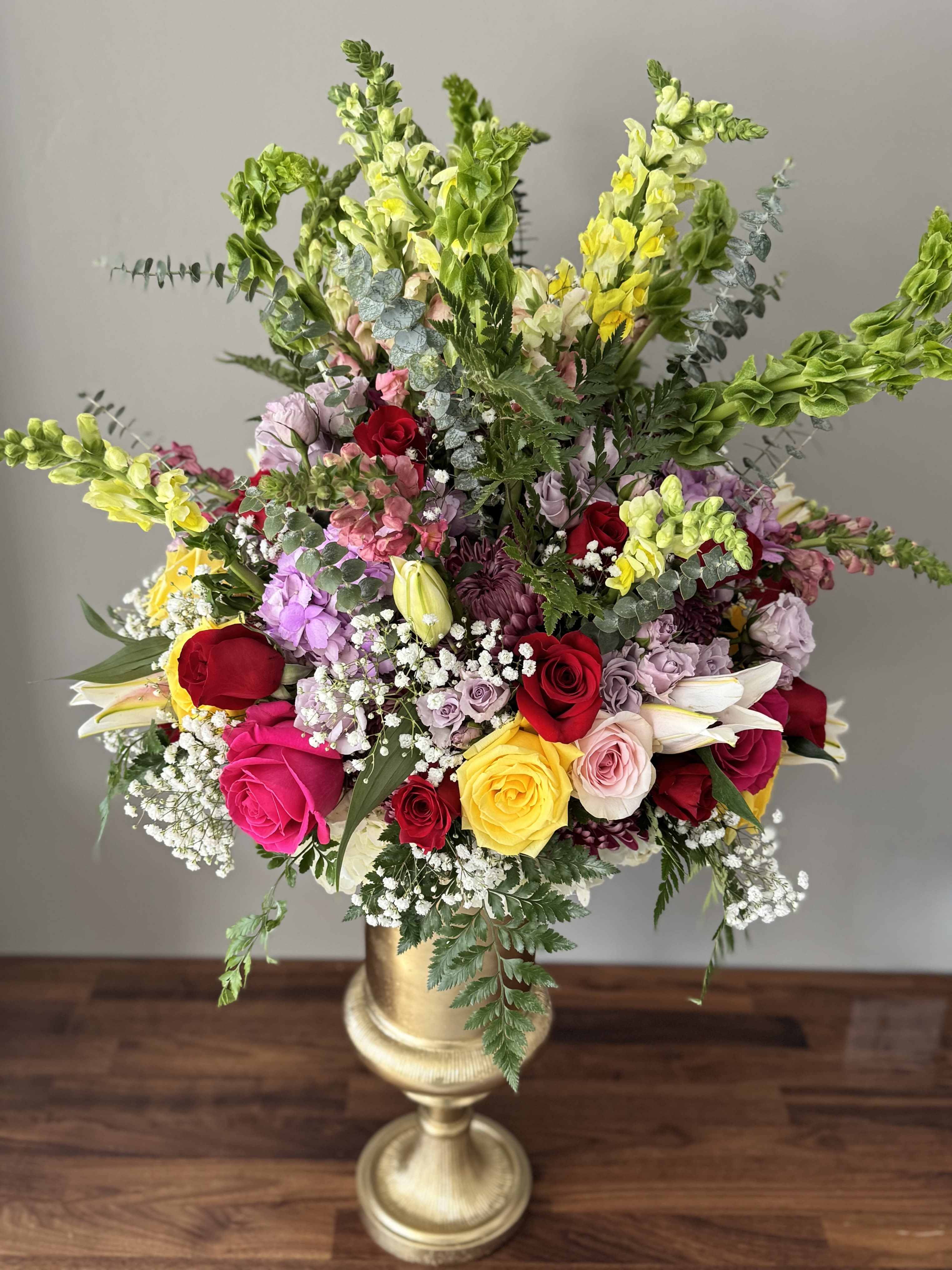 Large mixed flower arrangement in a gold pedestal vase