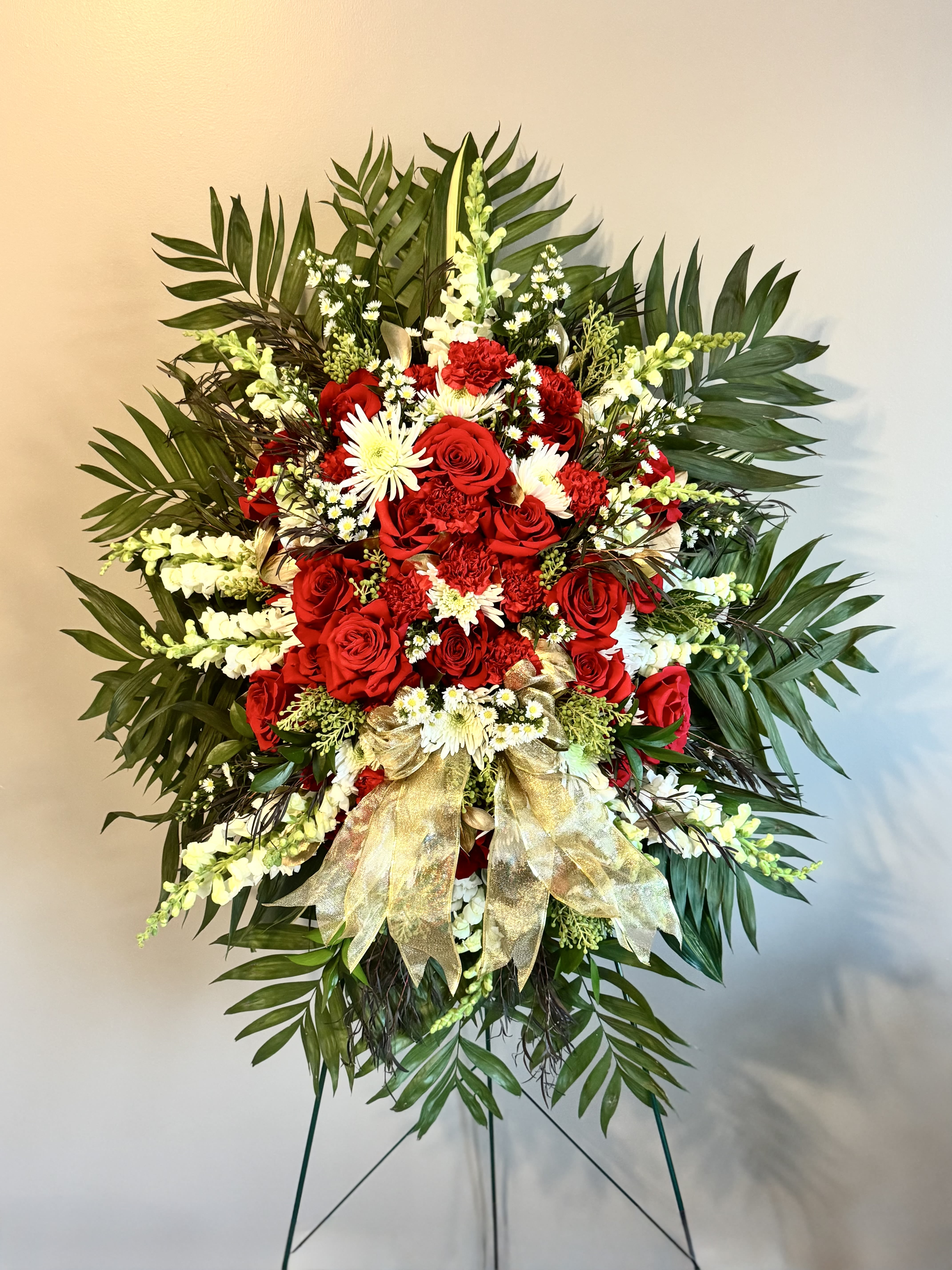 Standing floral spray with red roses and white flowers on a gold ribboned easel