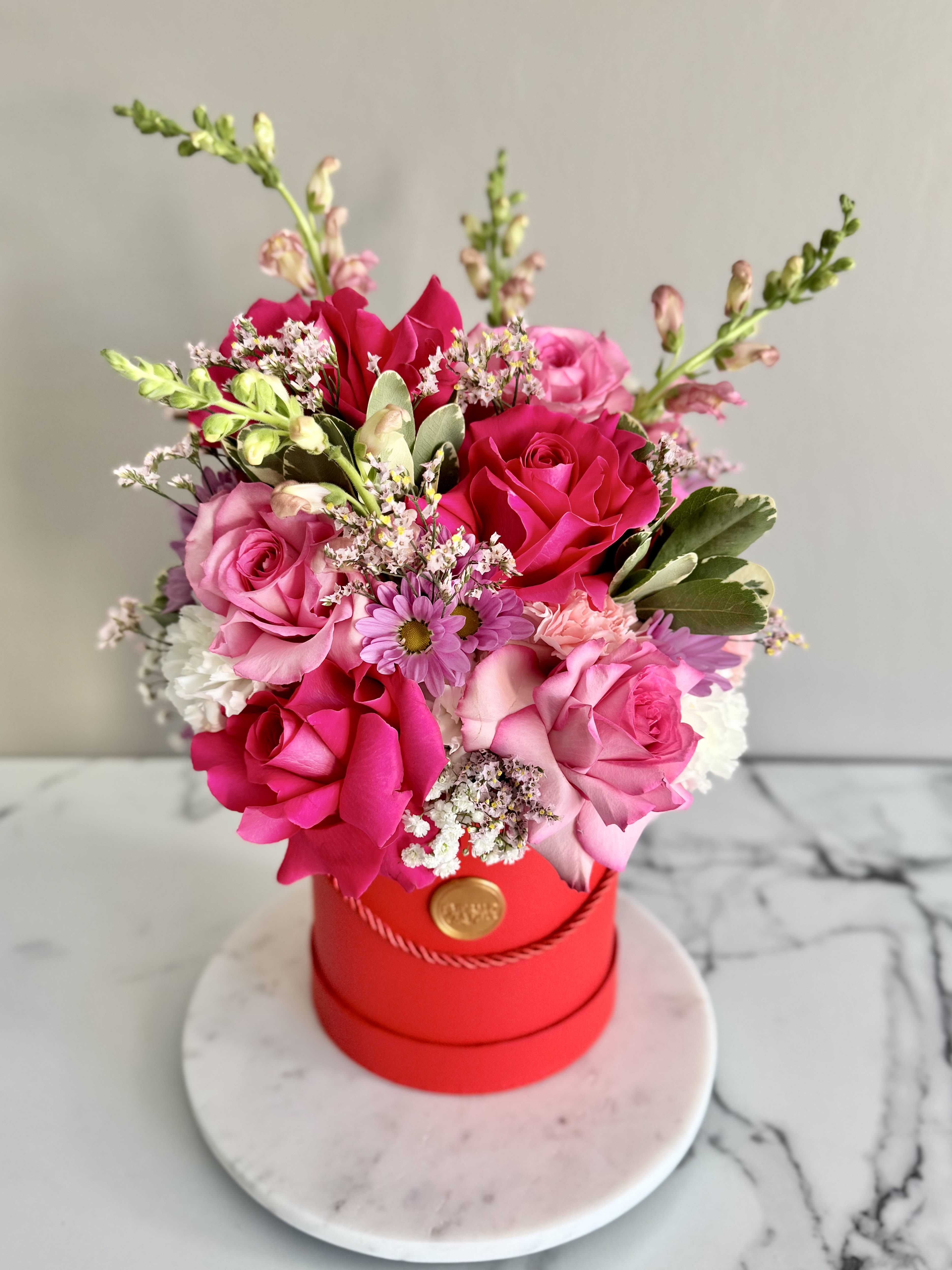 Pink and red rose bouquet in a red hat box on a round base