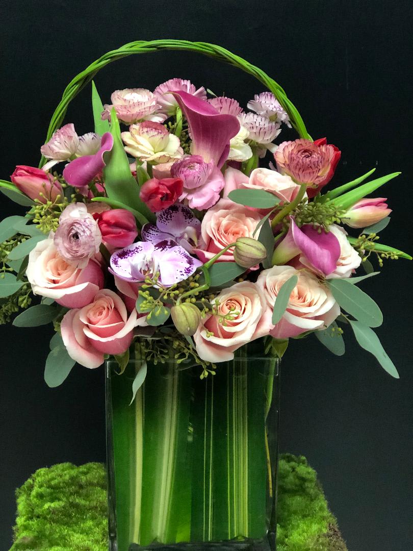 Pink and white floral arrangement in a tall glass vase with a green handle