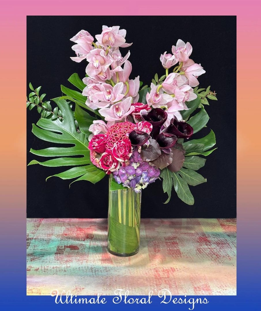 Pink orchids and mixed flowers arranged in a tall glass vase