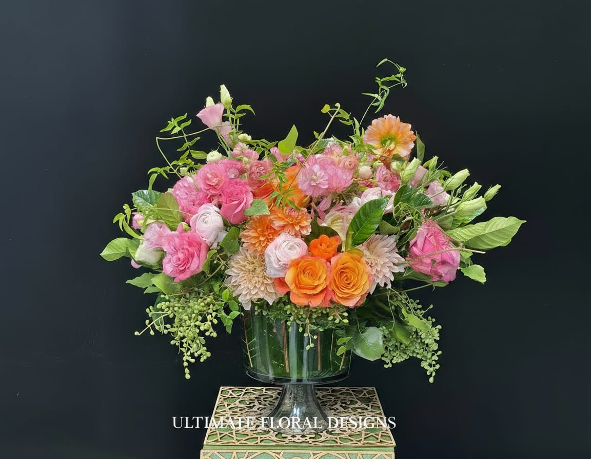 Pink and orange floral arrangement in a glass pedestal vase