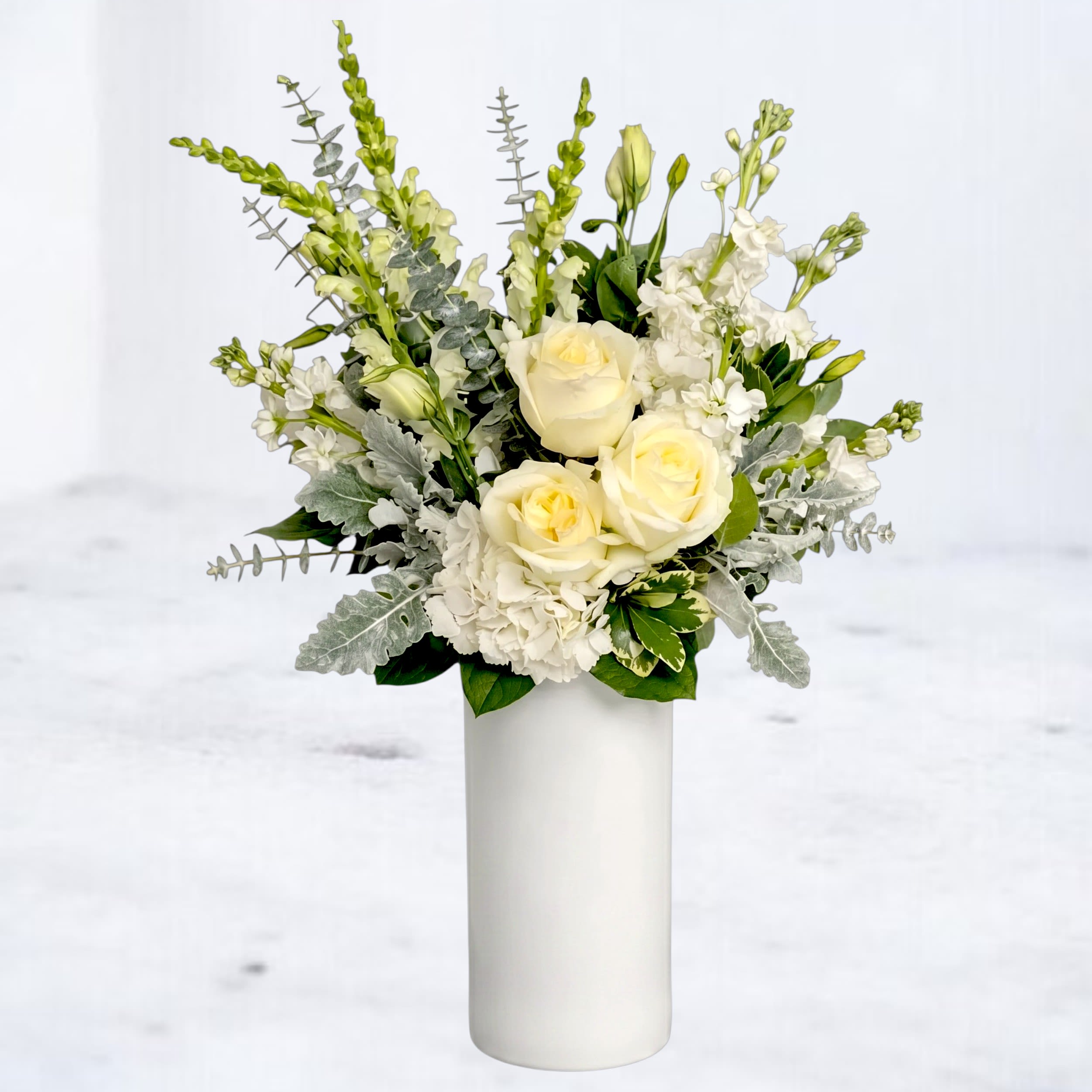 White roses and white flowers arranged in a tall white vase