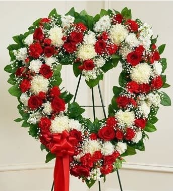 Heart-shaped wreath of red and white flowers on a stand with a red ribbon