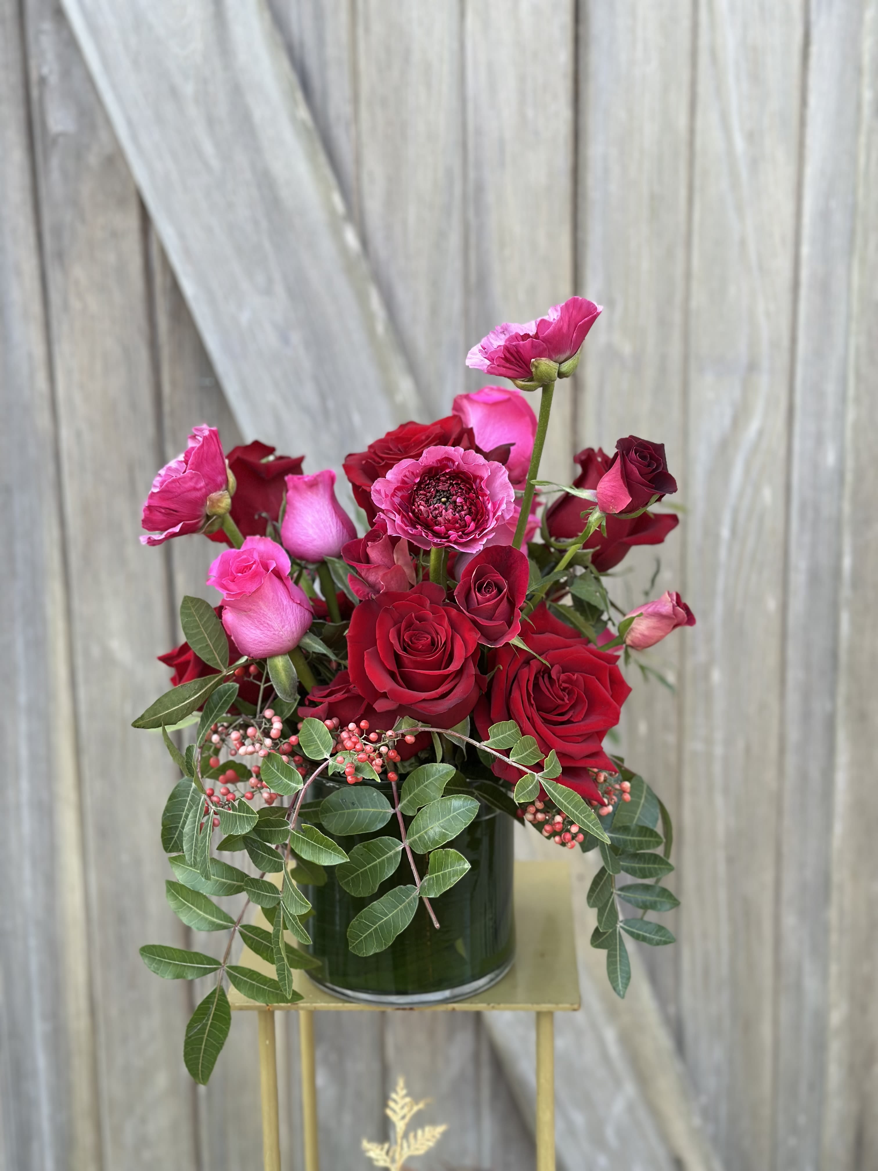 Red and pink roses arranged in a glass vase with trailing greenery.