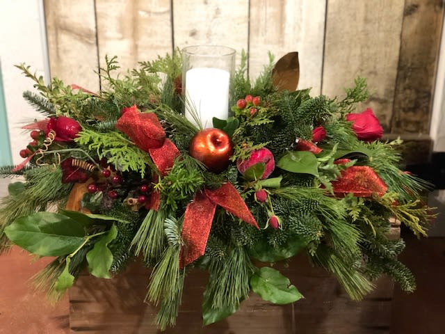 Holiday centerpiece with a white candle, red roses, and evergreen foliage