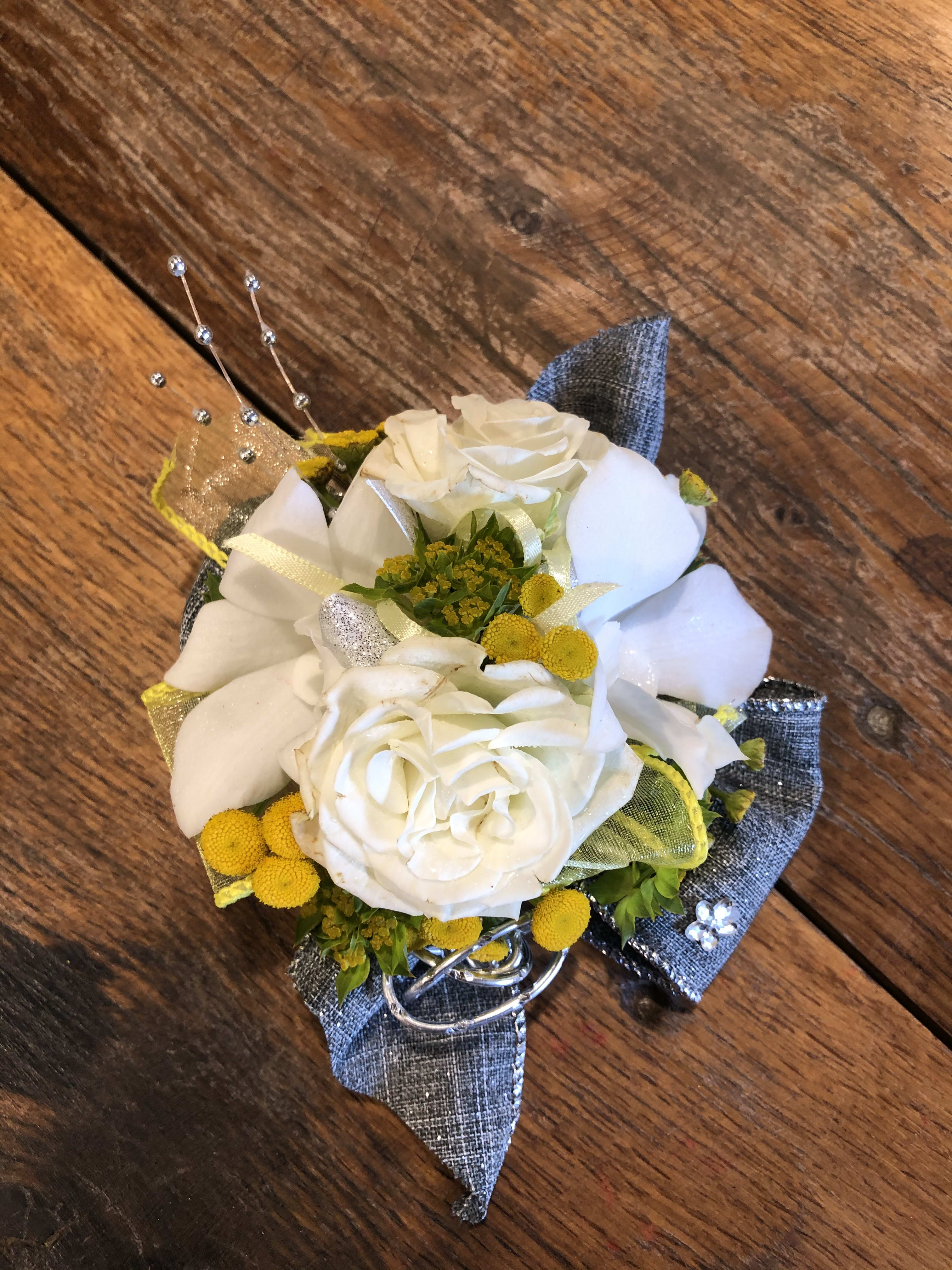 White rose corsage with yellow accents and silver ribbon on a wooden surface