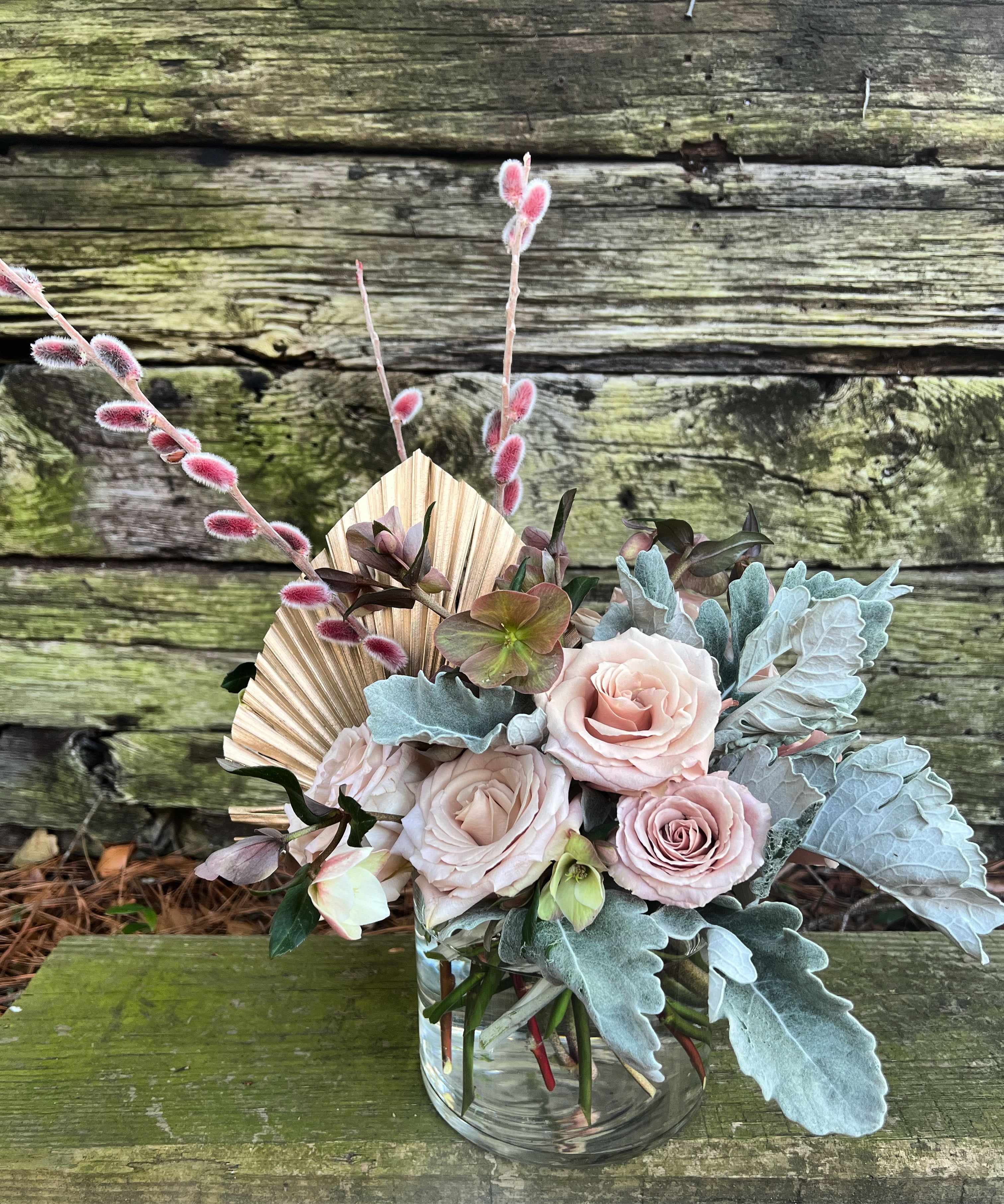 Blush roses in a clear glass vase with blue-gray foliage and pink pussy willow stems