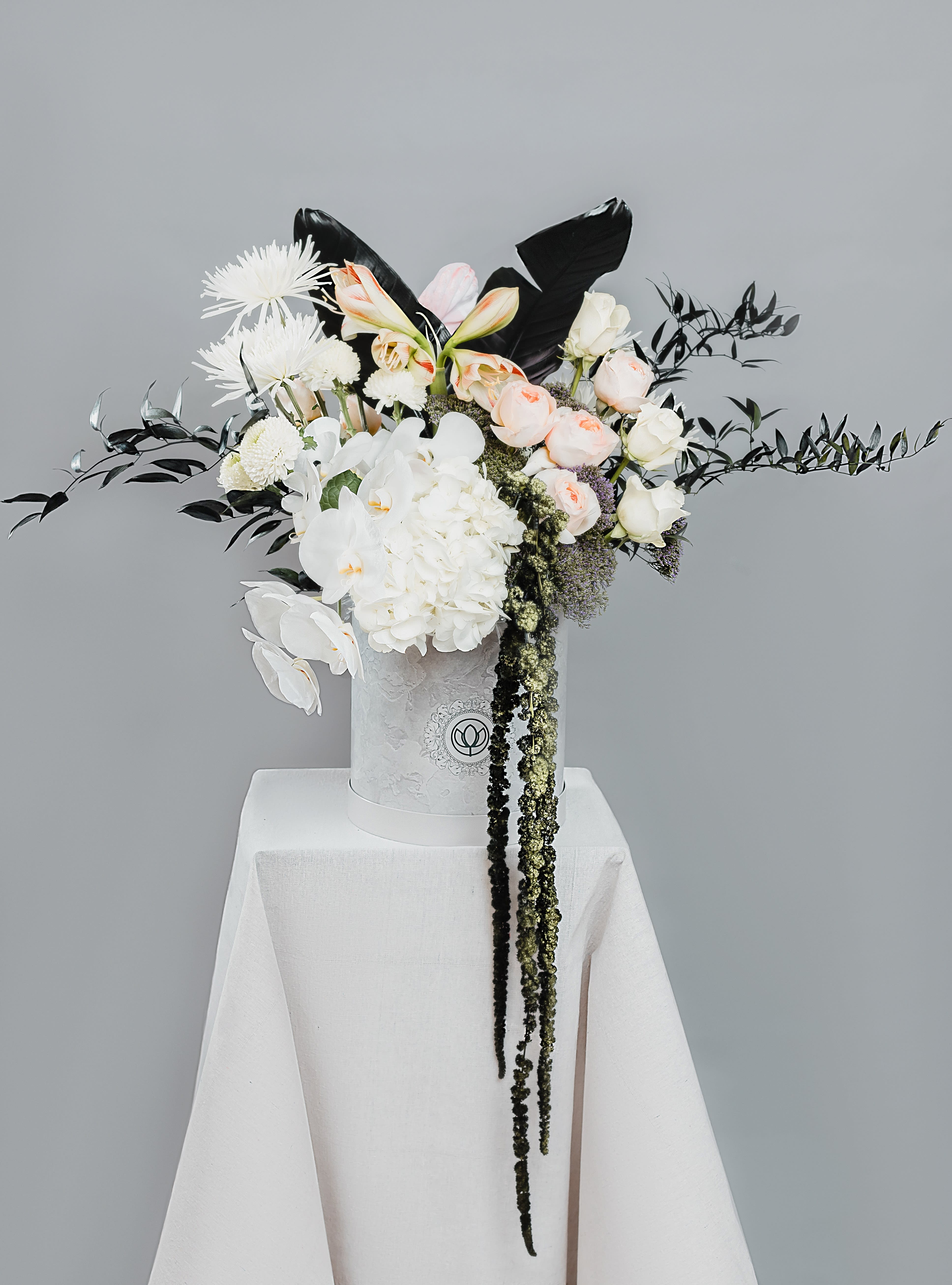 White and blush floral arrangement in a white hatbox on a draped pedestal