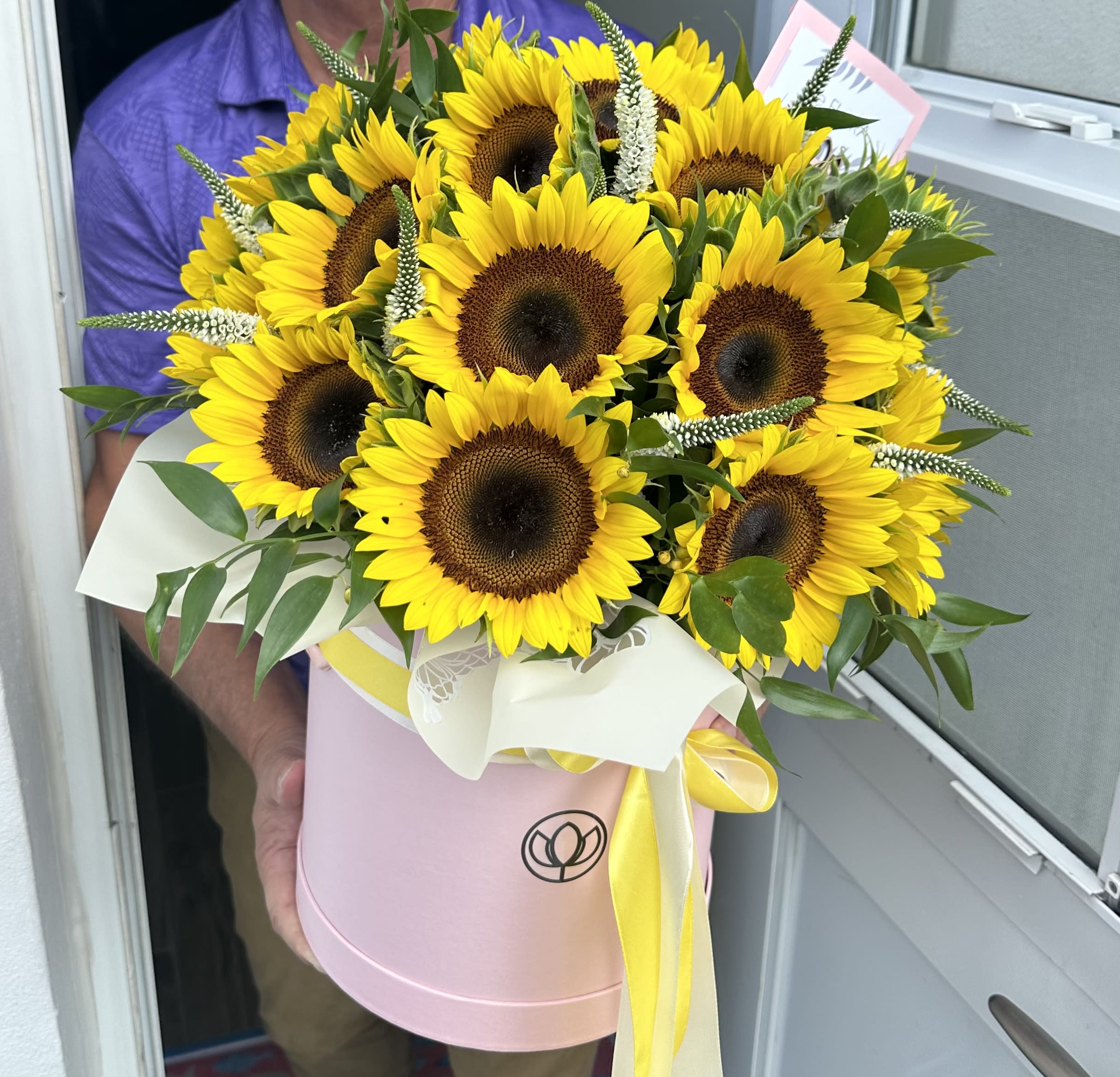 Bouquet of yellow sunflowers in a pink hatbox with a yellow ribbon