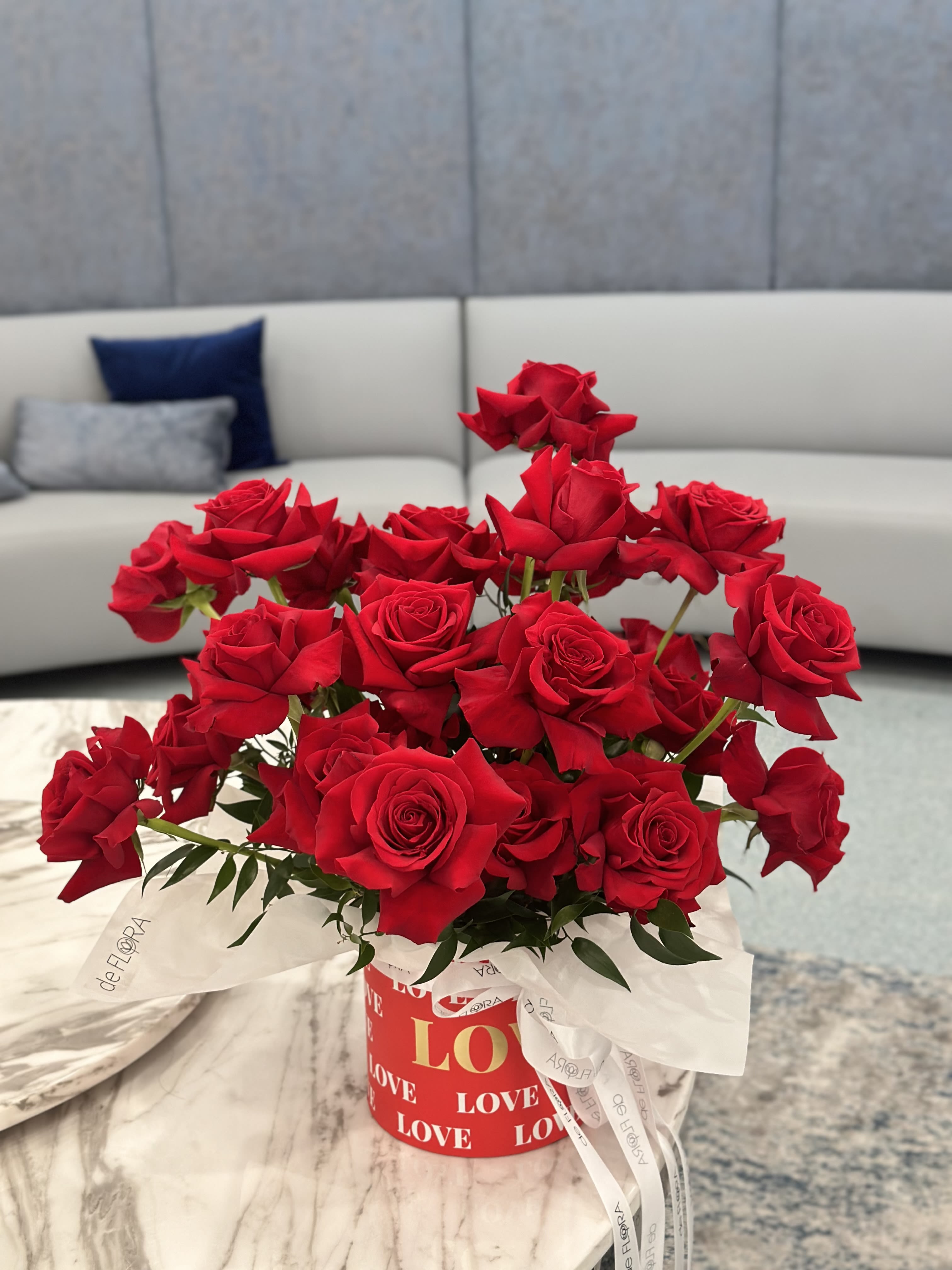 Red roses arranged in a round gift box with a white ribbon.