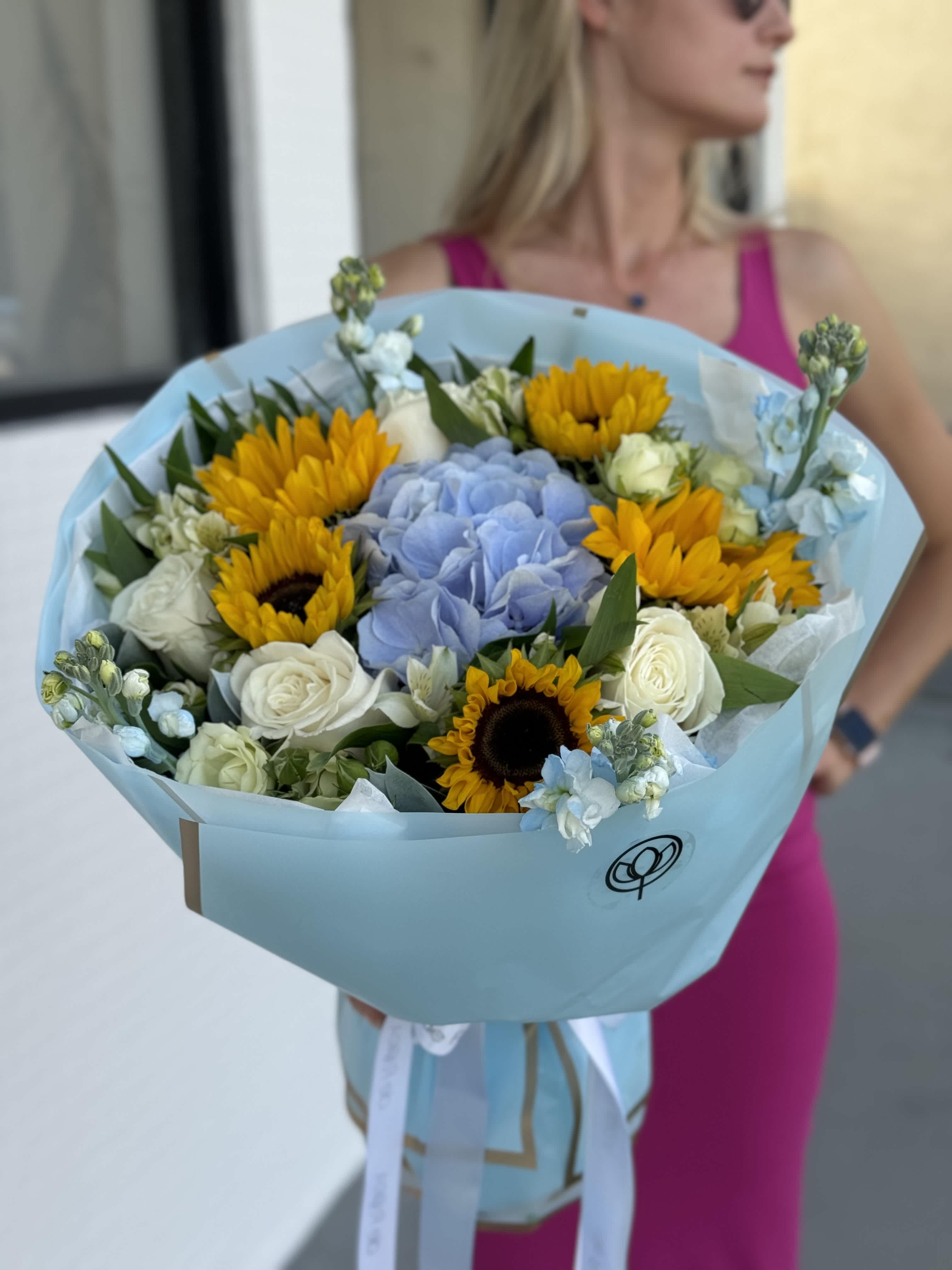 Bouquet of sunflowers, blue hydrangea, and white roses wrapped in pale blue paper