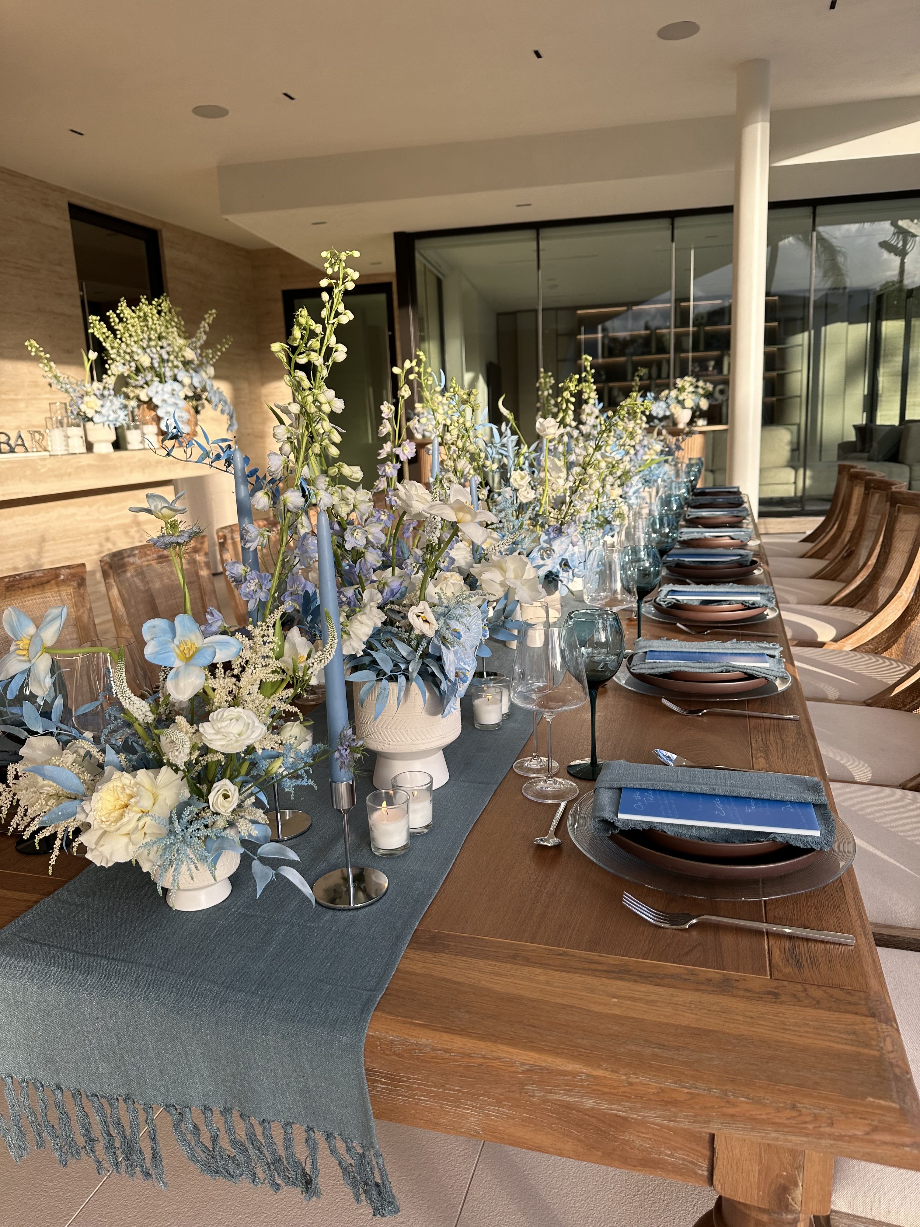 Blue and white floral centerpieces on a long dining table with candles and place settings