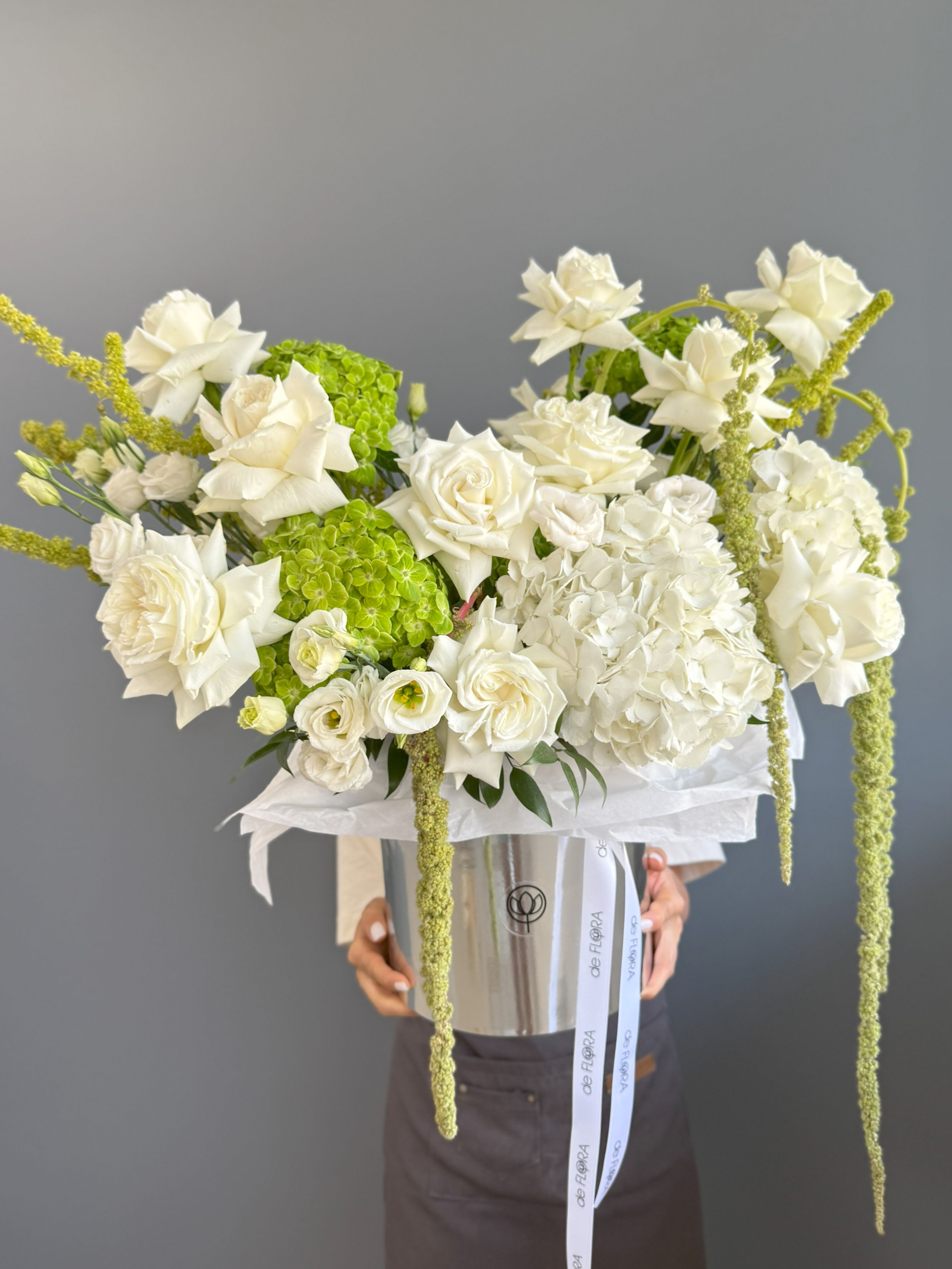 Large arrangement of white roses and hydrangeas with green accents in a silver hatbox container.