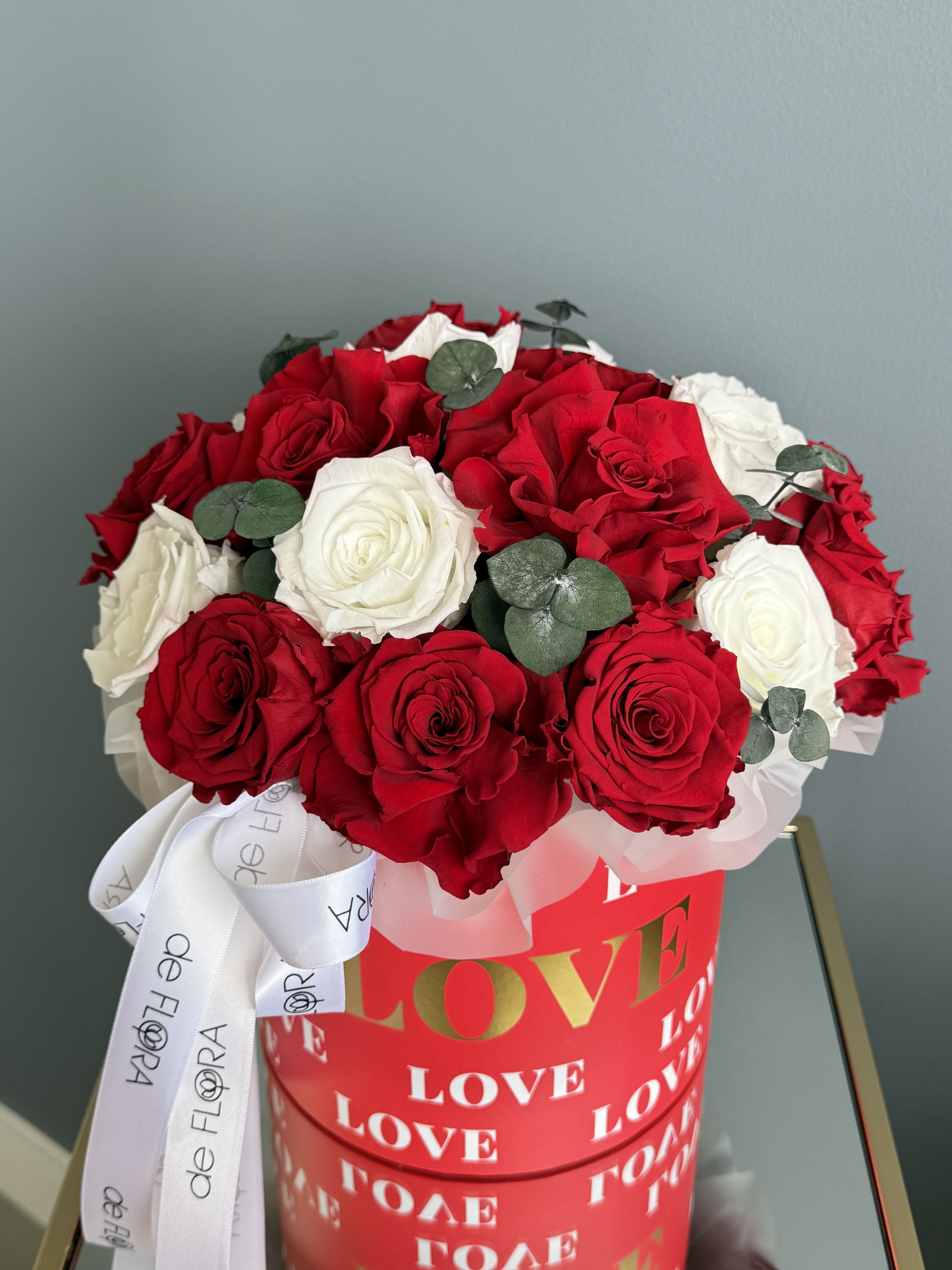 Red and white roses in a red heart-themed box with a white ribbon