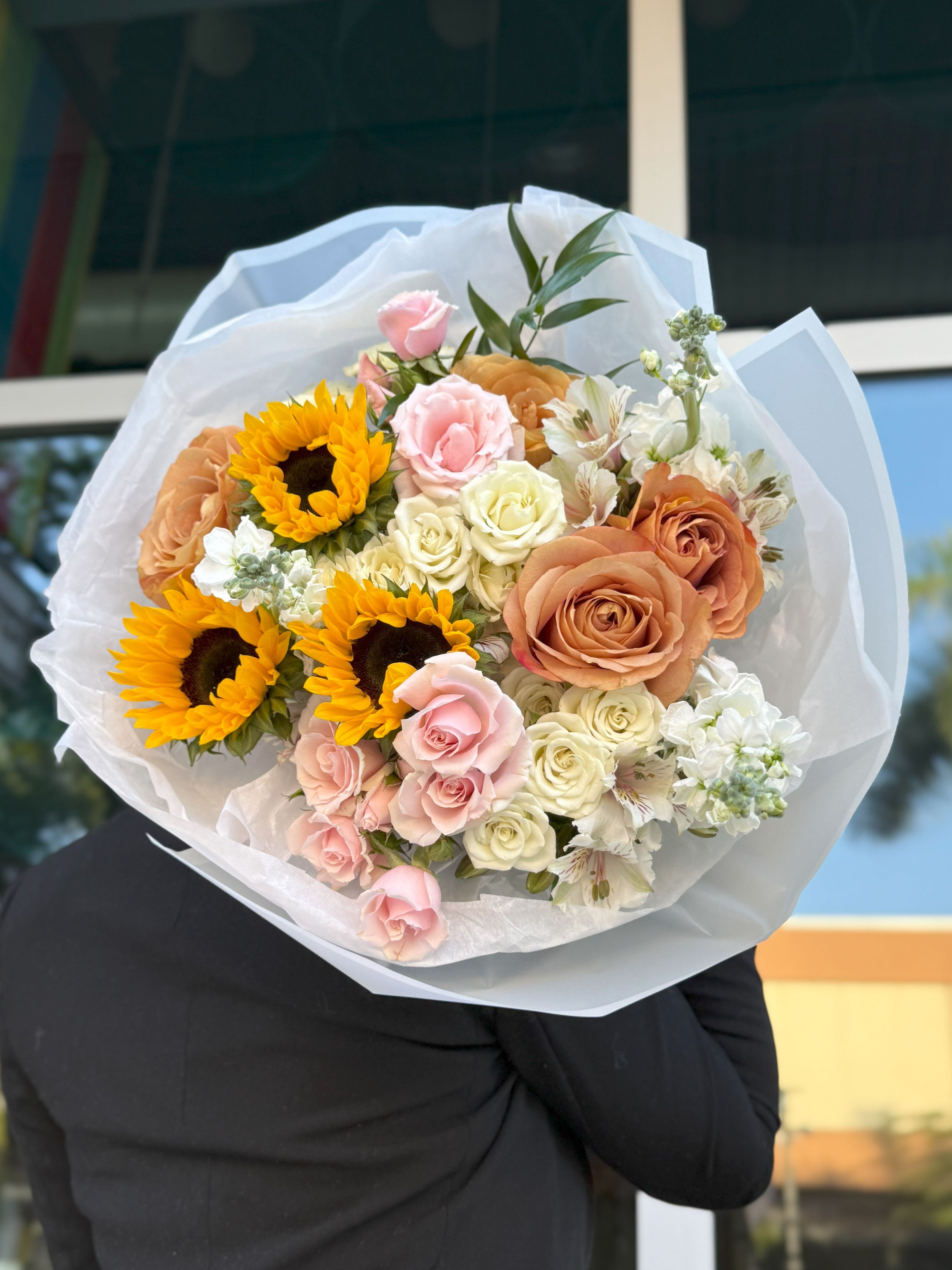 Bouquet of sunflowers, roses, and white flowers wrapped in white paper