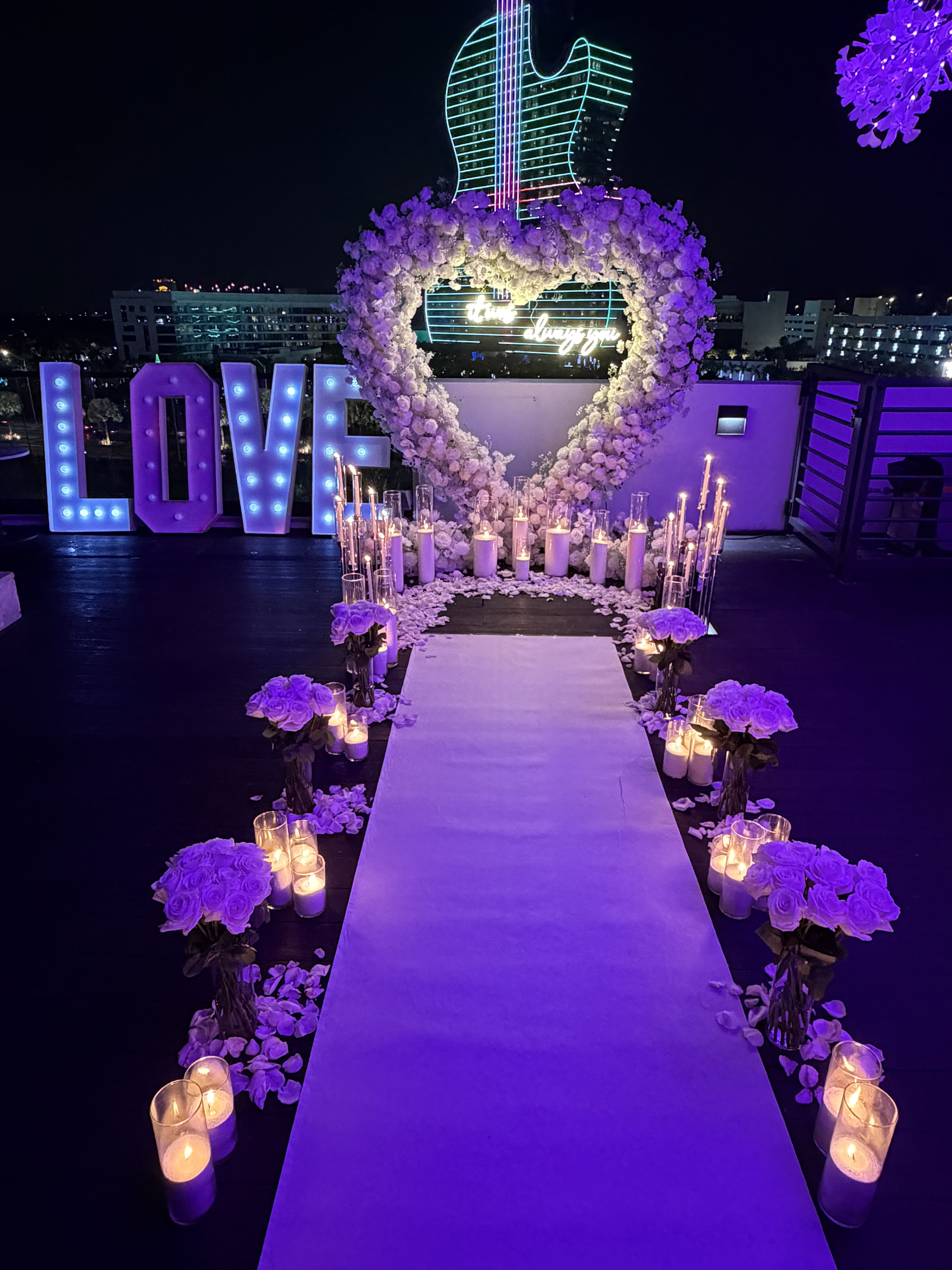 Purple floral wedding aisle with heart arch, candles, and lit LOVE sign