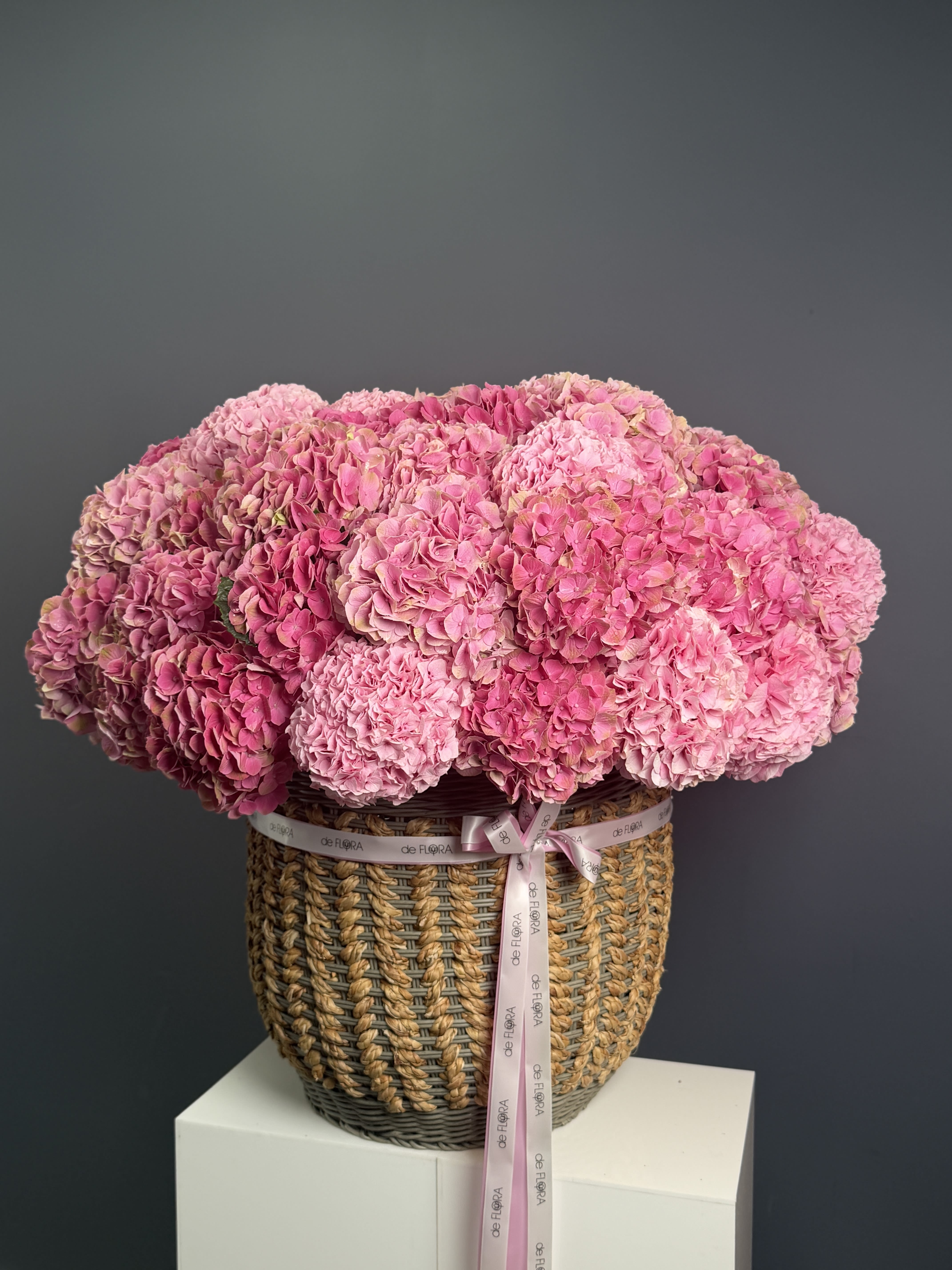 Blush Hydrangea Garden - A soft, romantic statement piece featuring lush premium hydrangeas in layered shades of blush, rose, and dusty pink. Arranged in a handwoven basket and finished with a signature deFLORA ribbon, this design feels both natural and elevated.  Full, cloud-like blooms create a rich, voluminous look — perfect for elegant home décor, heartfelt gifts, or sophisticated celebrations.  Timeless, feminine, and effortlessly luxurious.