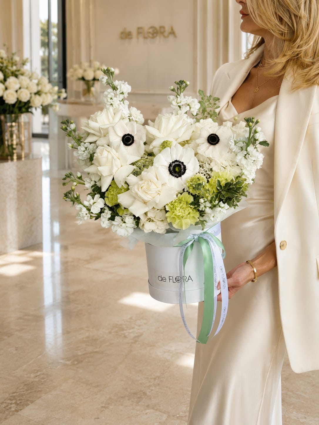 White Mixed Flower Box with Roses - An exquisite arrangement of creamy white roses, delicate anemones with deep contrasting centers, soft green hydrangea, and airy seasonal blooms, thoughtfully designed in a signature deFLORA hat box.  This refined composition celebrates purity, elegance, and calm beauty. The harmony of ivory, soft green, and natural textures creates a timeless floral statement, finished with a pastel satin ribbon for a perfect final touch.  Ideal for weddings, anniversaries, congratulations, newborn celebrations, and moments that call for understated luxury.