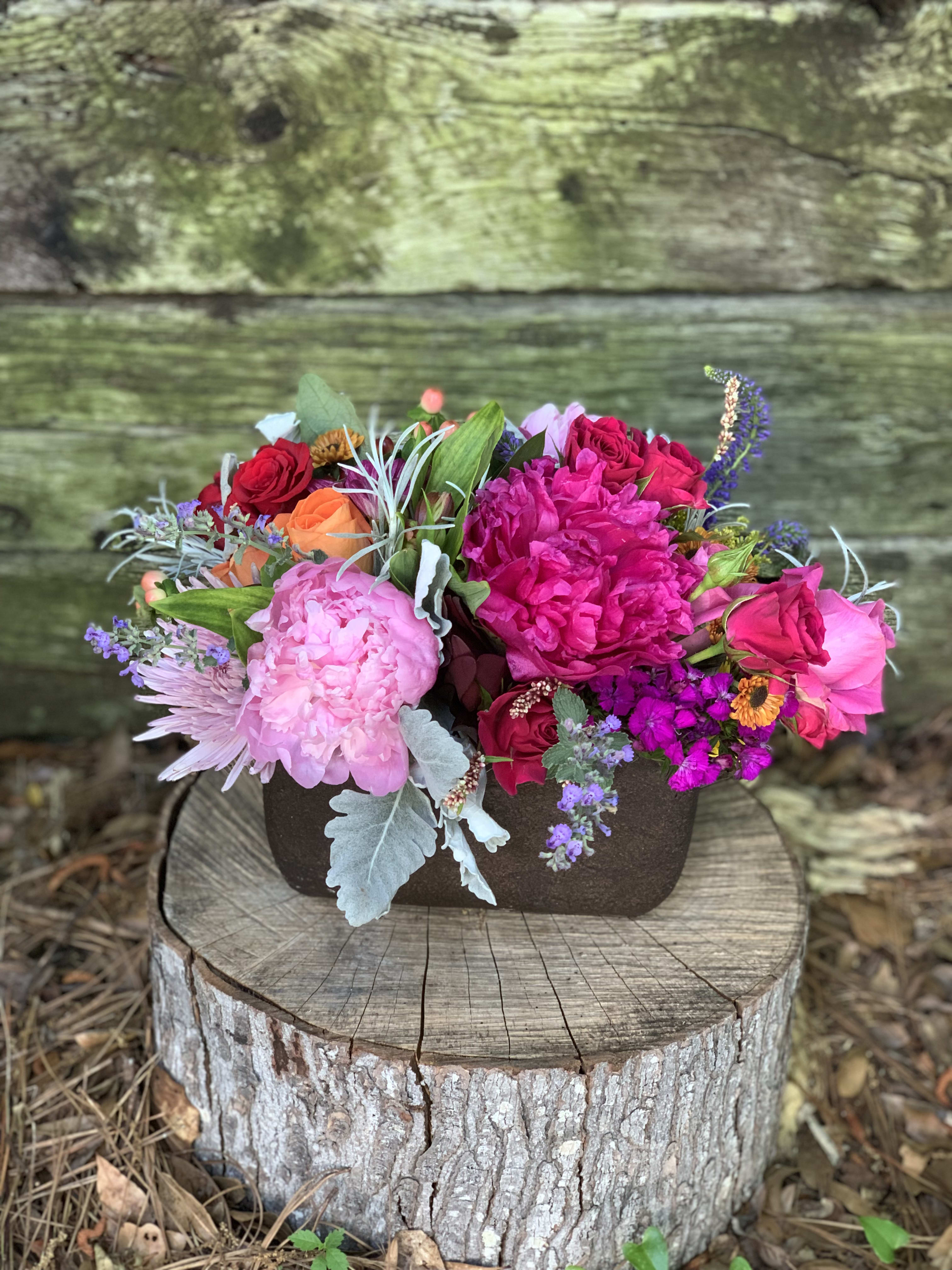 Mixed bouquet of pink, red, and orange flowers in a dark container