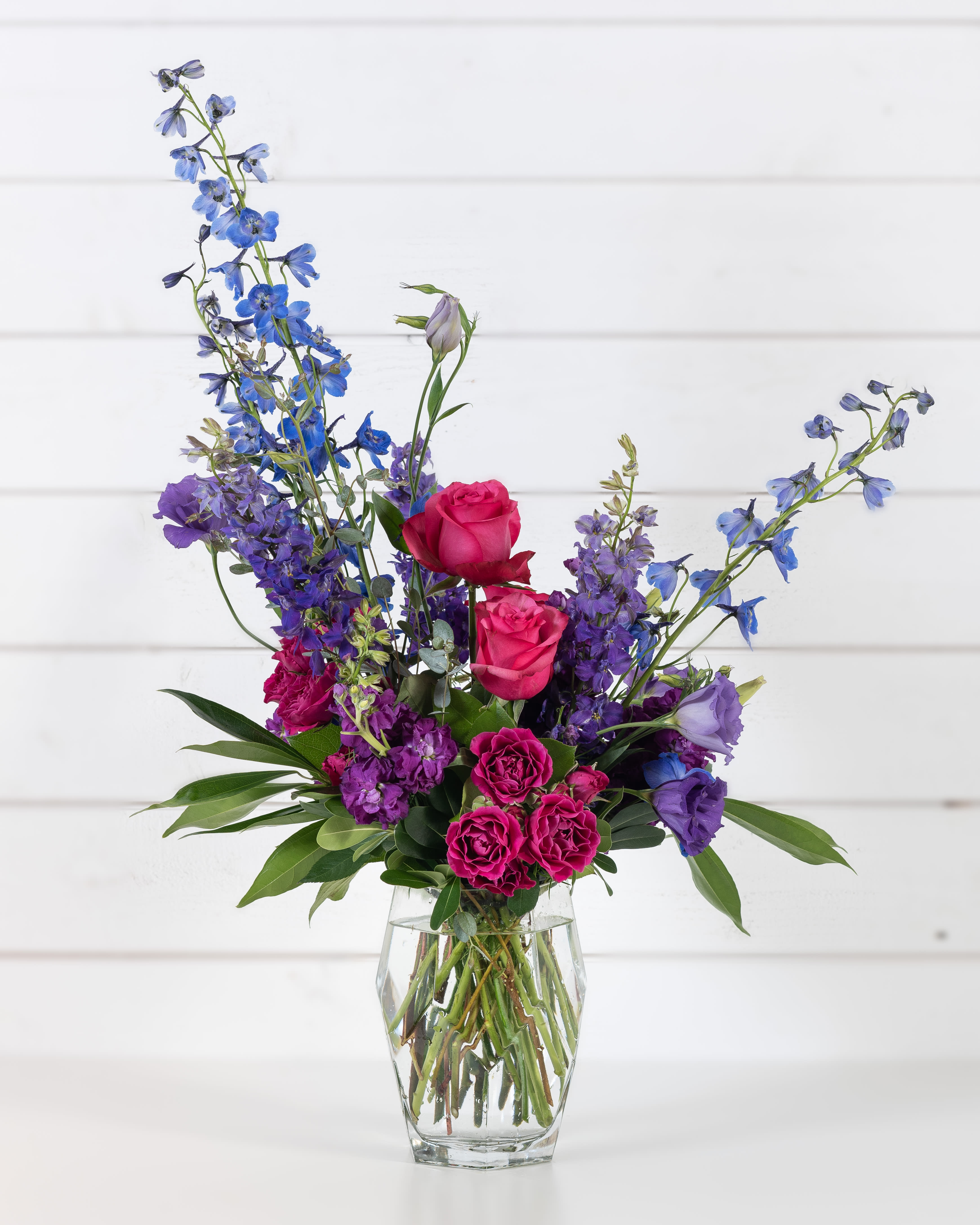 Mixed bouquet of pink roses and blue-purple flowers in a clear glass vase