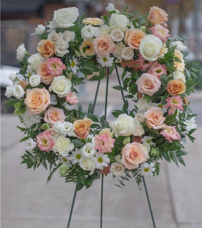 Circular floral wreath on a stand with white, peach, and pink blooms
