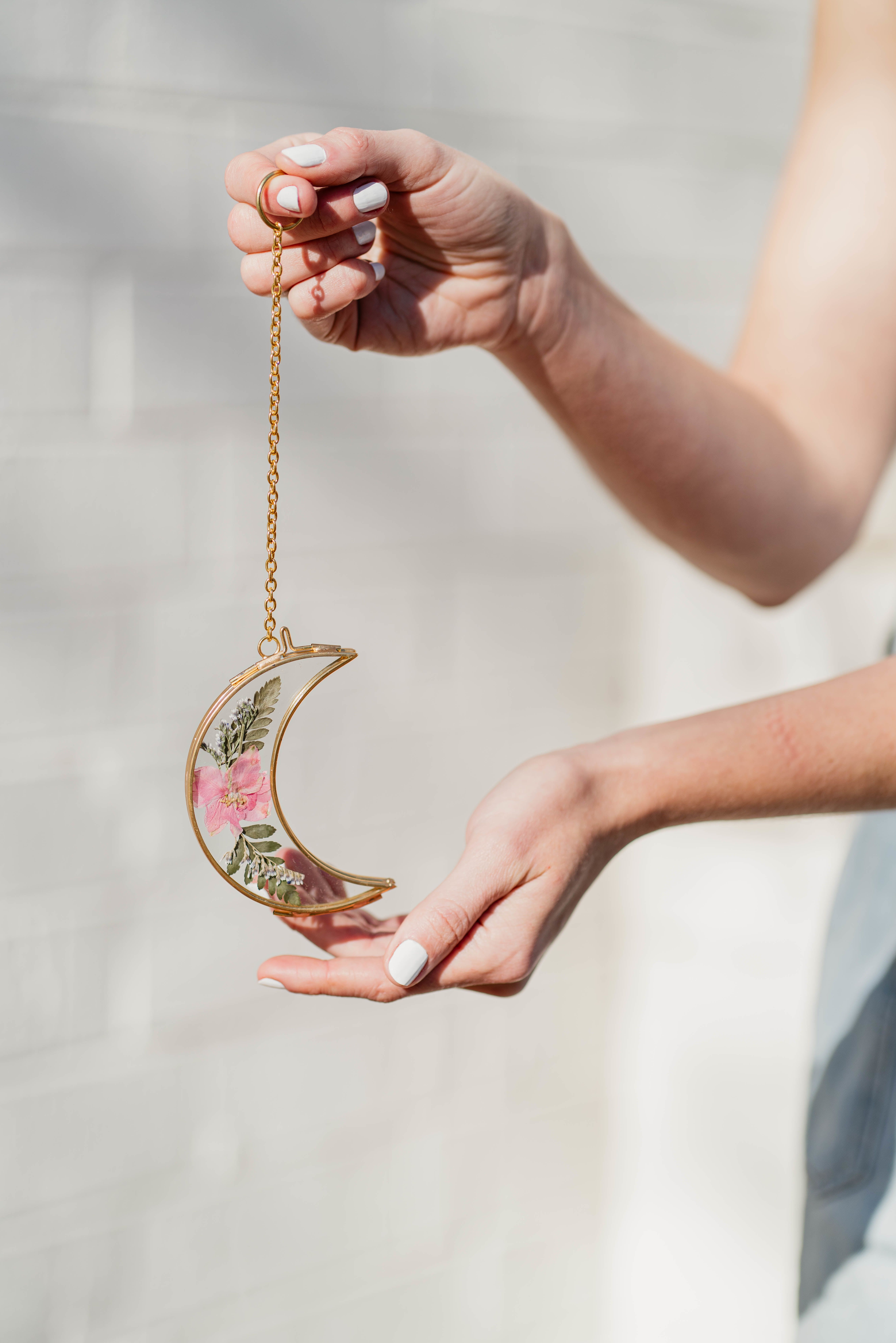 Hands holding a crescent moon ornament with pressed flowers