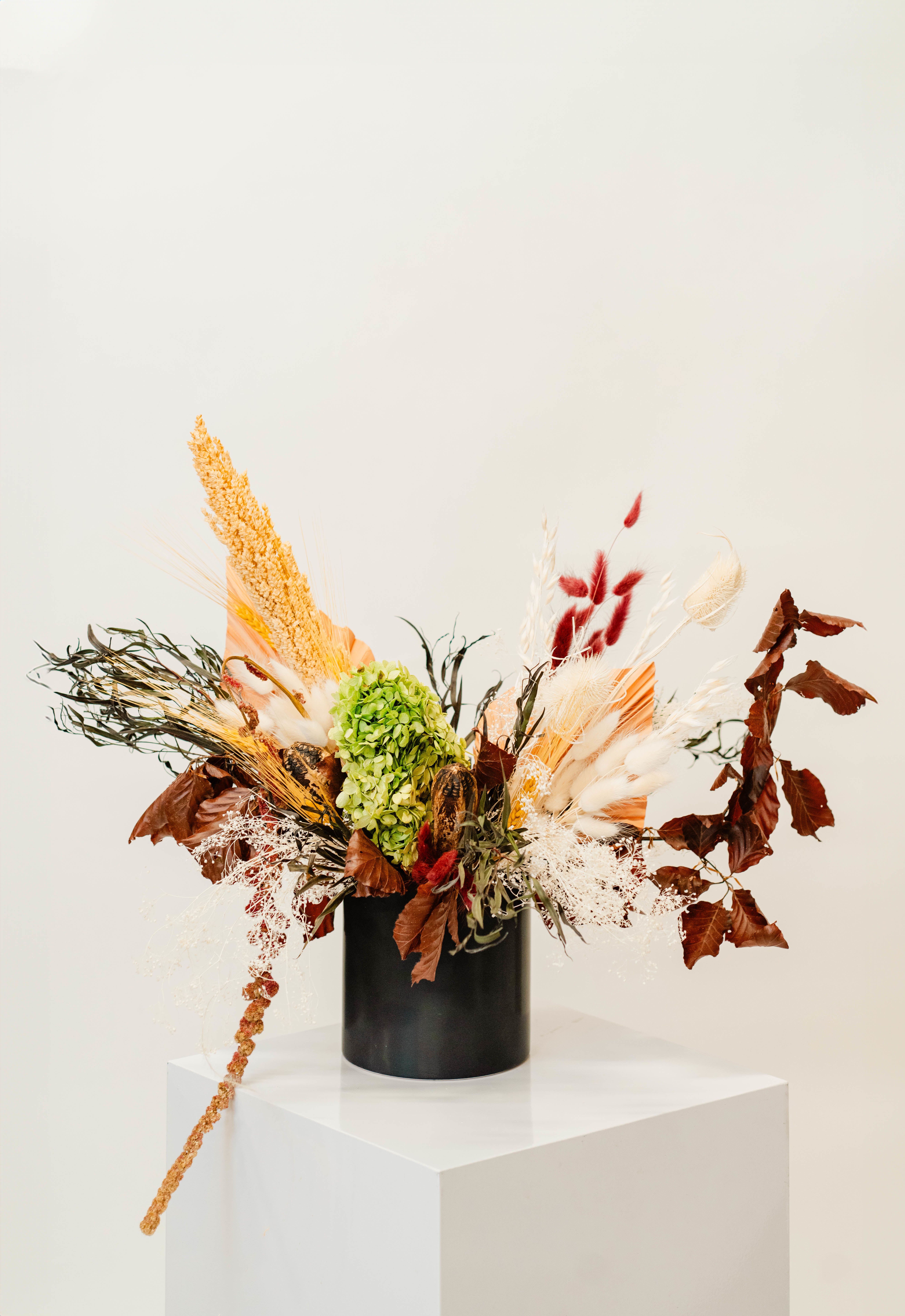 Dried floral arrangement in a black vase with green hydrangea and tan, white, and red accents