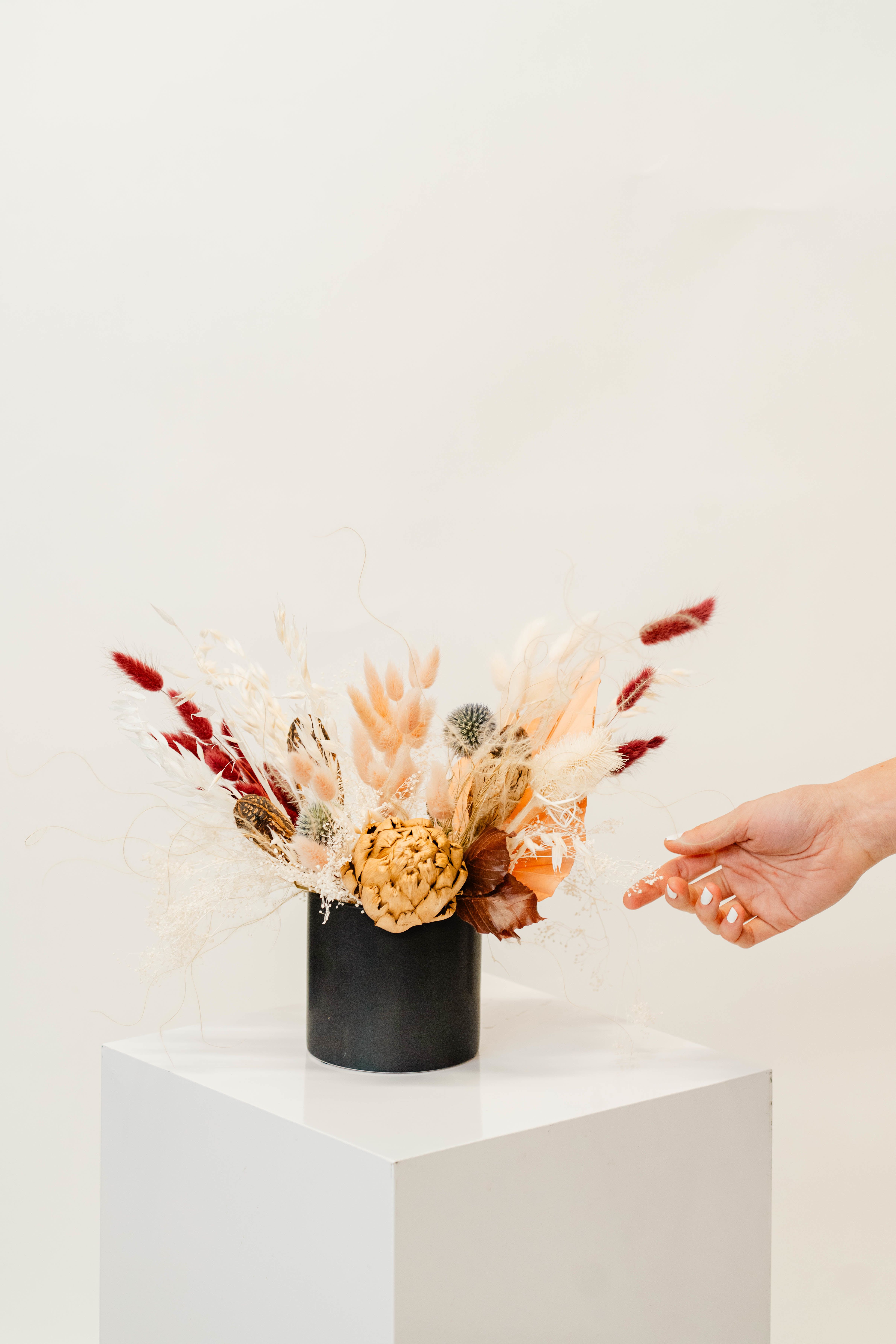 Dried floral arrangement in a black vase with red and cream accents