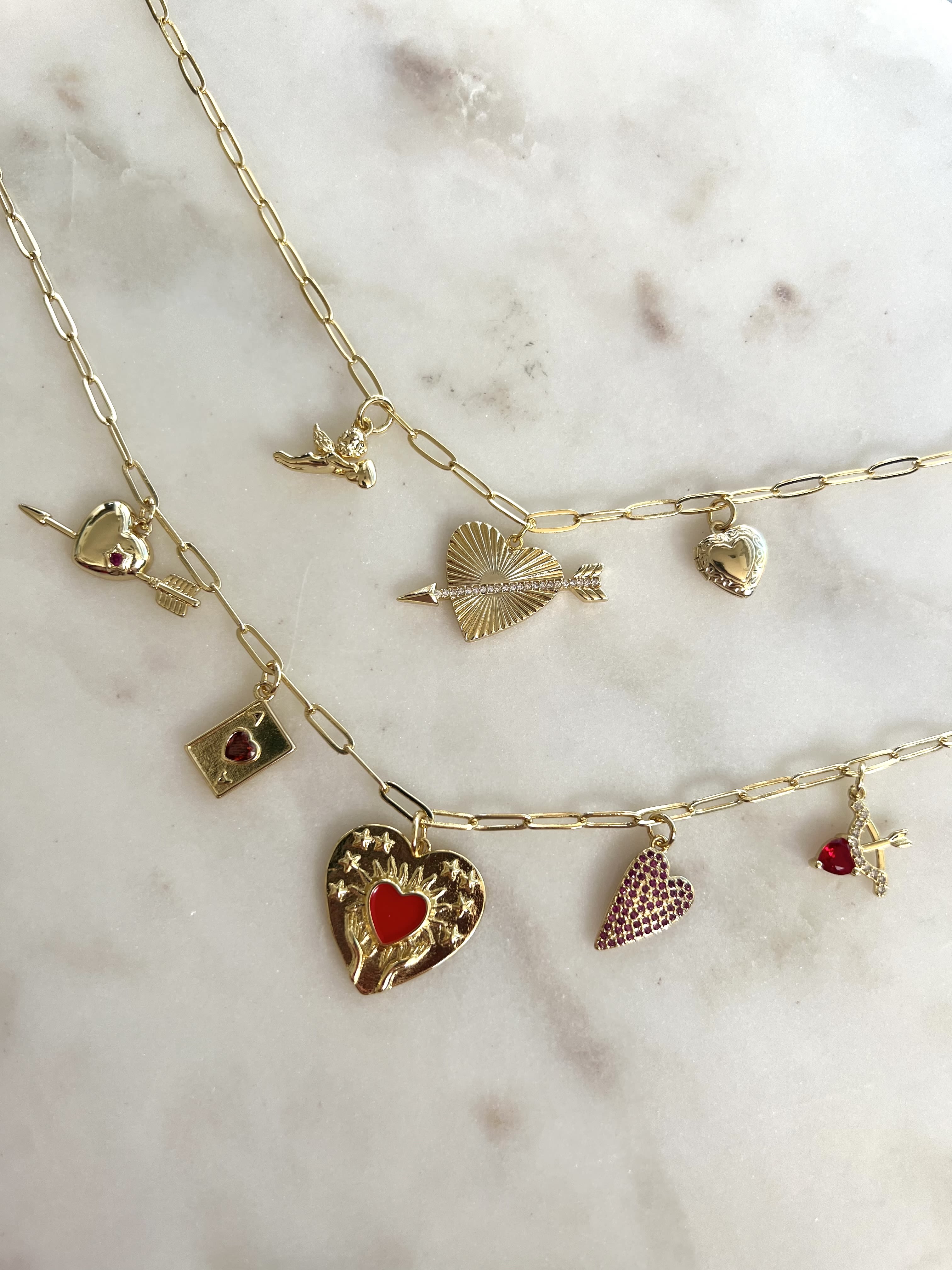 Gold charm necklaces with heart and arrow pendants on a marble surface