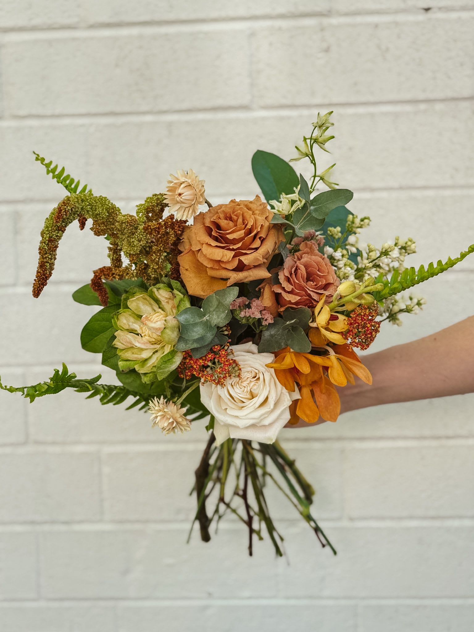 Handheld bouquet of orange, white, and green flowers