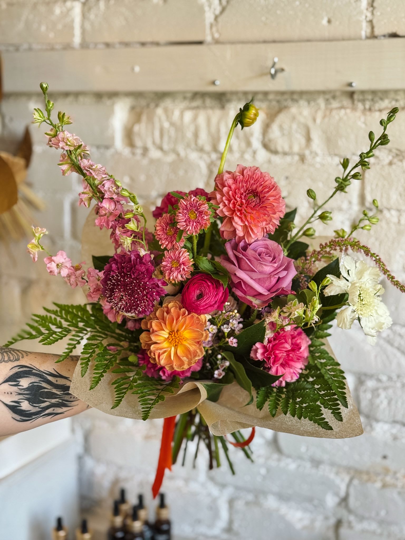 Hand-tied bouquet of pink, orange, and white flowers wrapped in paper