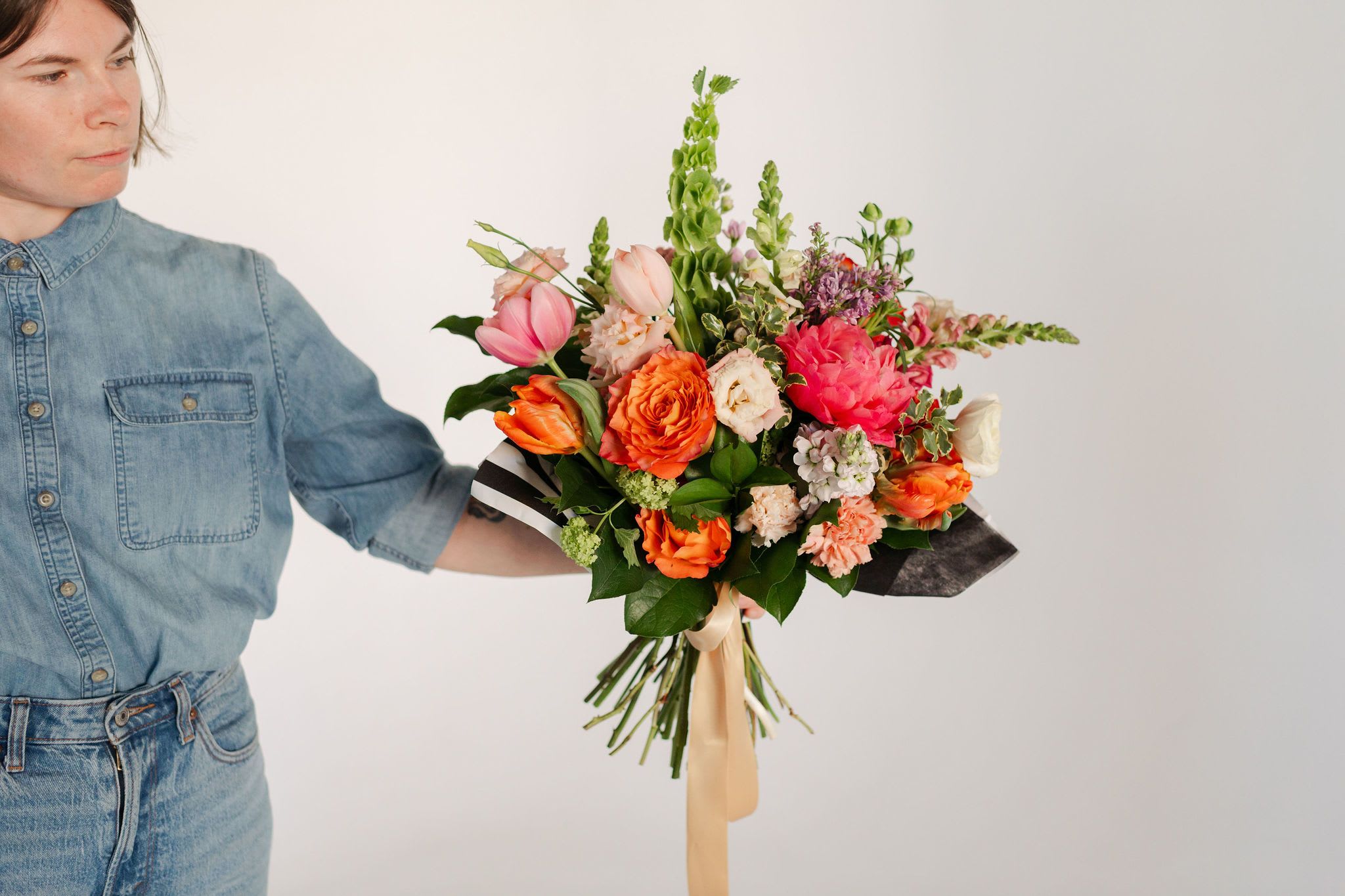 Summer Sunshine Deluxe Hand-Tied Bouquet - A stunning, premium hand-tied arrangement including coral charm peonies, fluffy lisianthus, lush parrot tulips and sculptural bells of Ireland enhanced with dramatic snapdragons, fragrant stock and fresh greenery.  