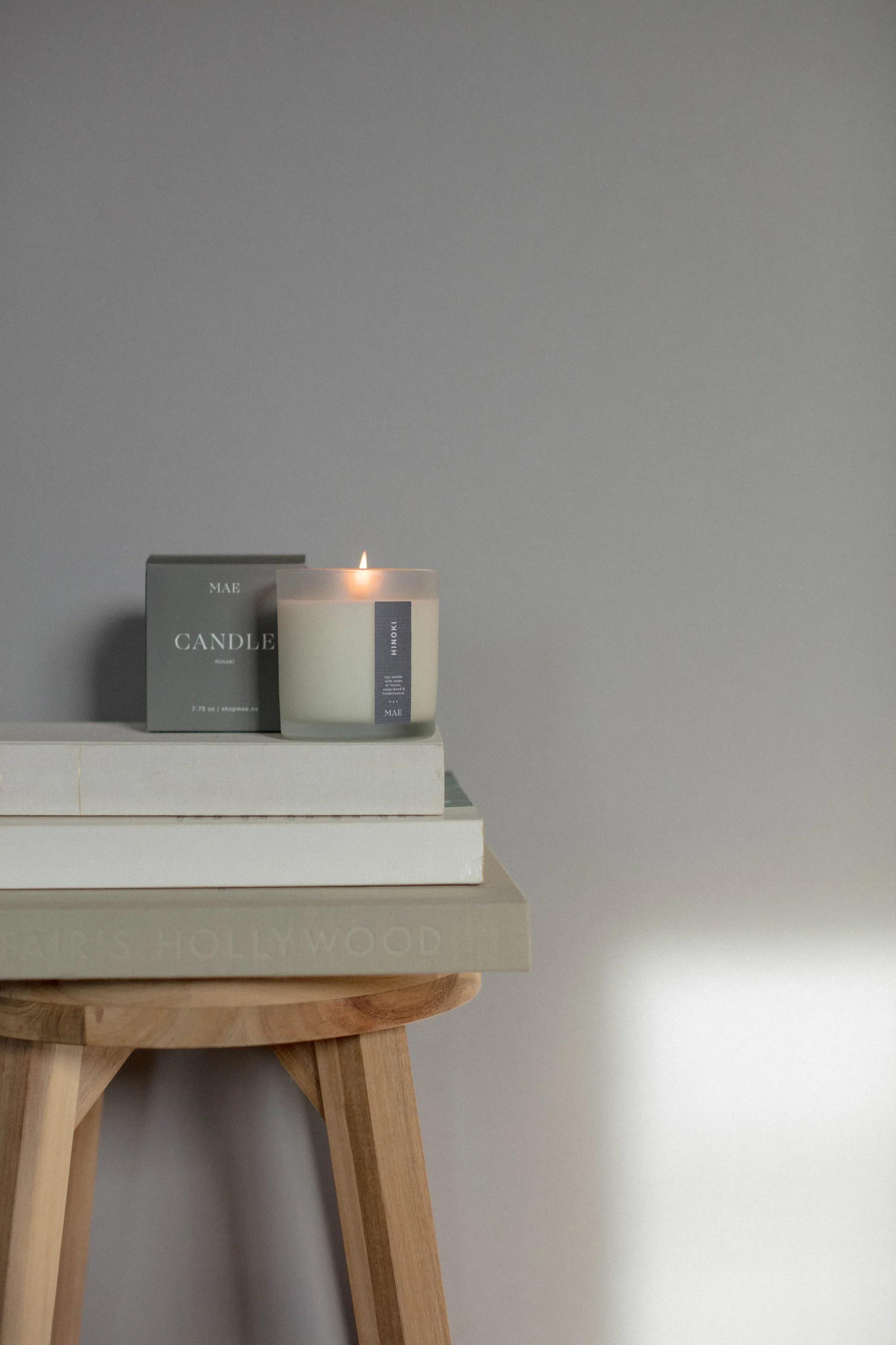 Lit candle in a glass jar beside its box on stacked books