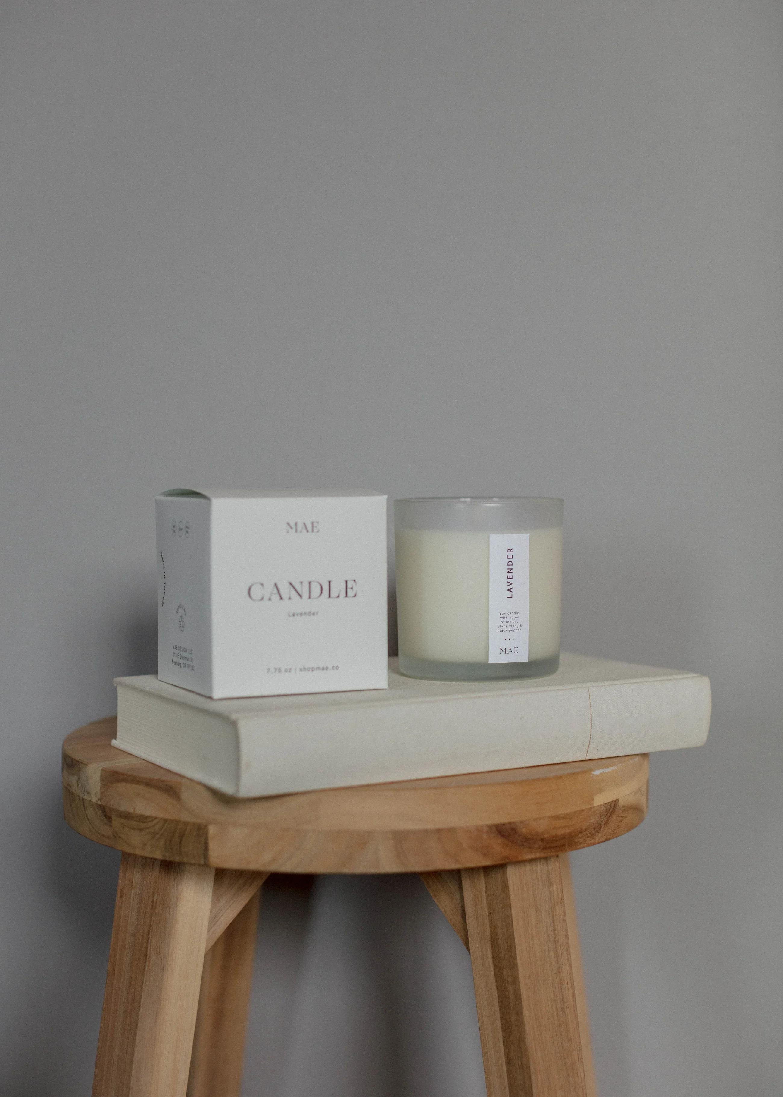 Lavender candle in a glass jar beside its white box on a wooden stool