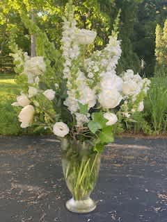 Tall white floral arrangement in a clear glass vase outdoors