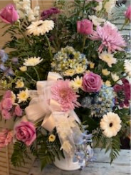 Summer Sentiments - This white funeral urn consists of full mixed bouquet layers roses, gerbera-style daisies, chrysanthemums, alstroemeria, snapdragons, and smaller daisy and filler blooms for a lush, garden-inspired silhouette. The palette of pink, white, purple, and soft blue creates gentle contrast and texture - rounded rose heads and chrysanthemum pompons against taller, spiky snapdragons - arranged in a generous, slightly elevated shape that reads both abundant and refined.