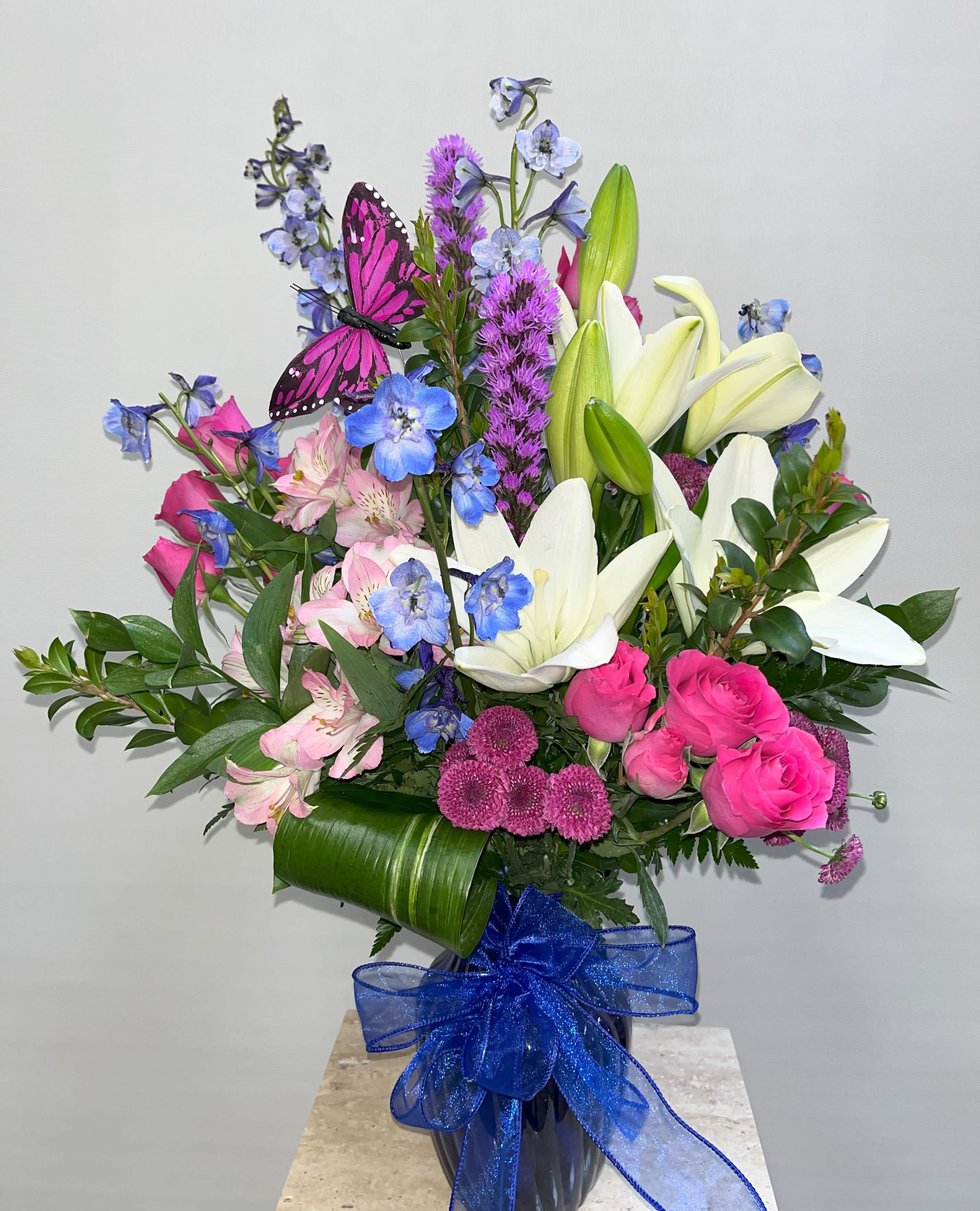 Bouquet of pink roses, white lilies, and blue flowers in a vase with a blue ribbon