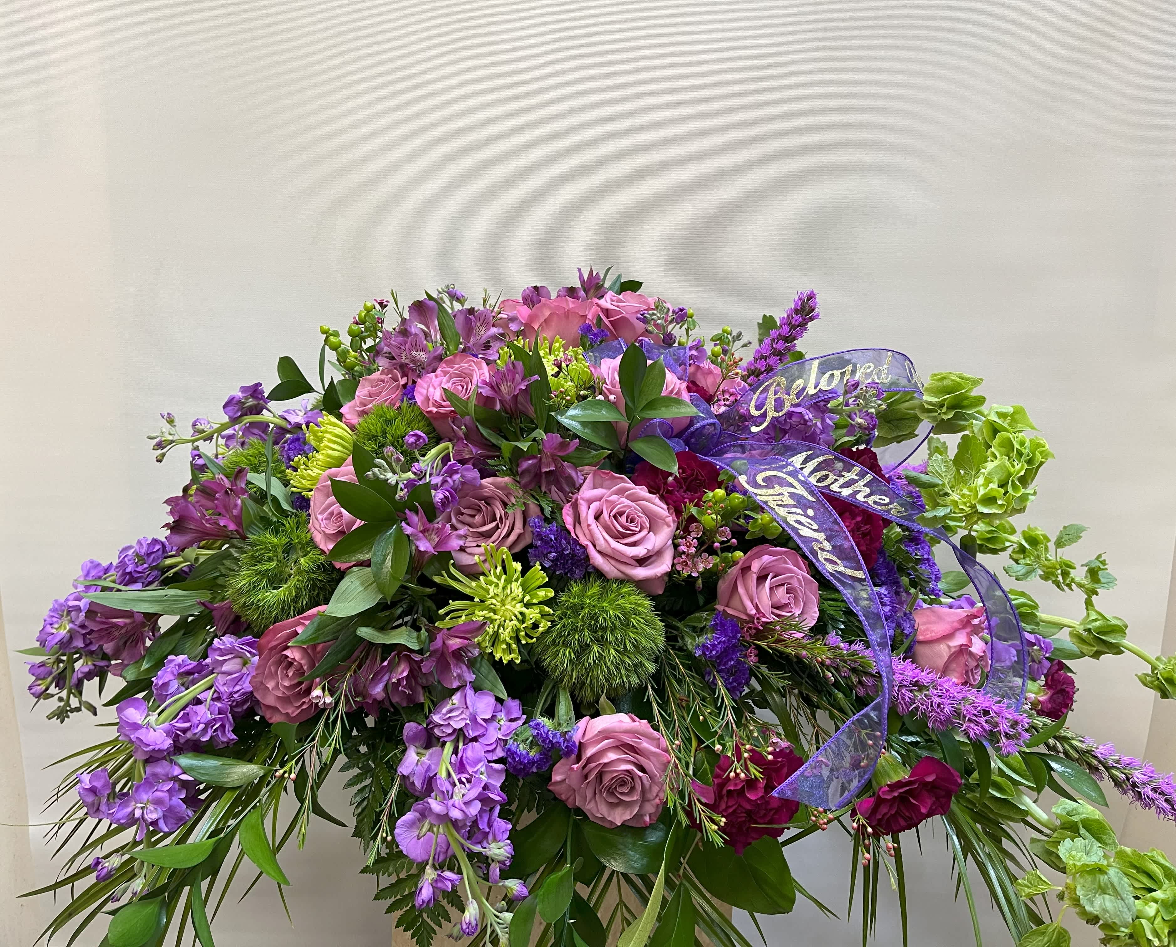 Large purple and pink floral spray with ribbon on a stand