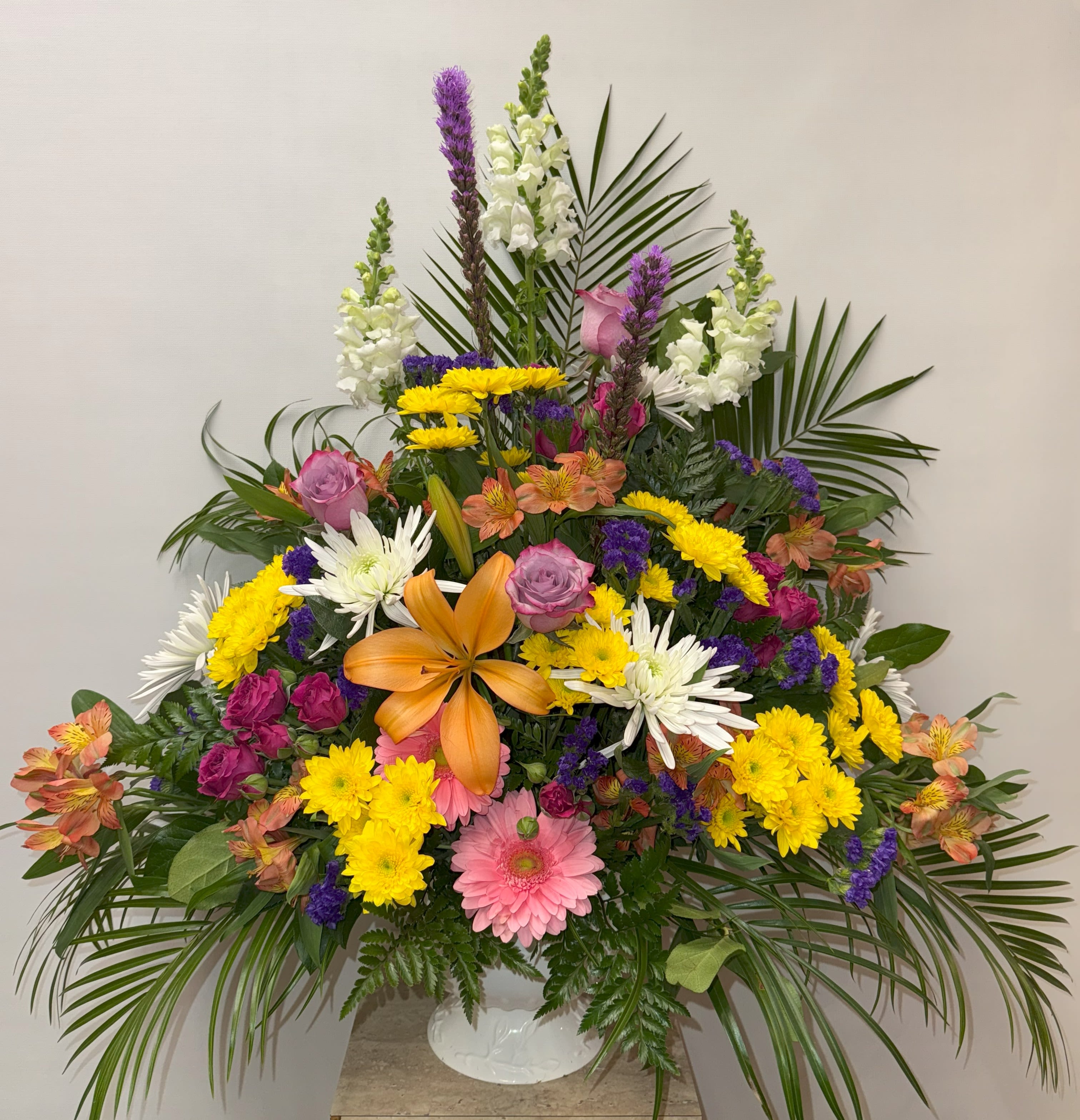 Large mixed flower arrangement in a white vase with lilies and daisies