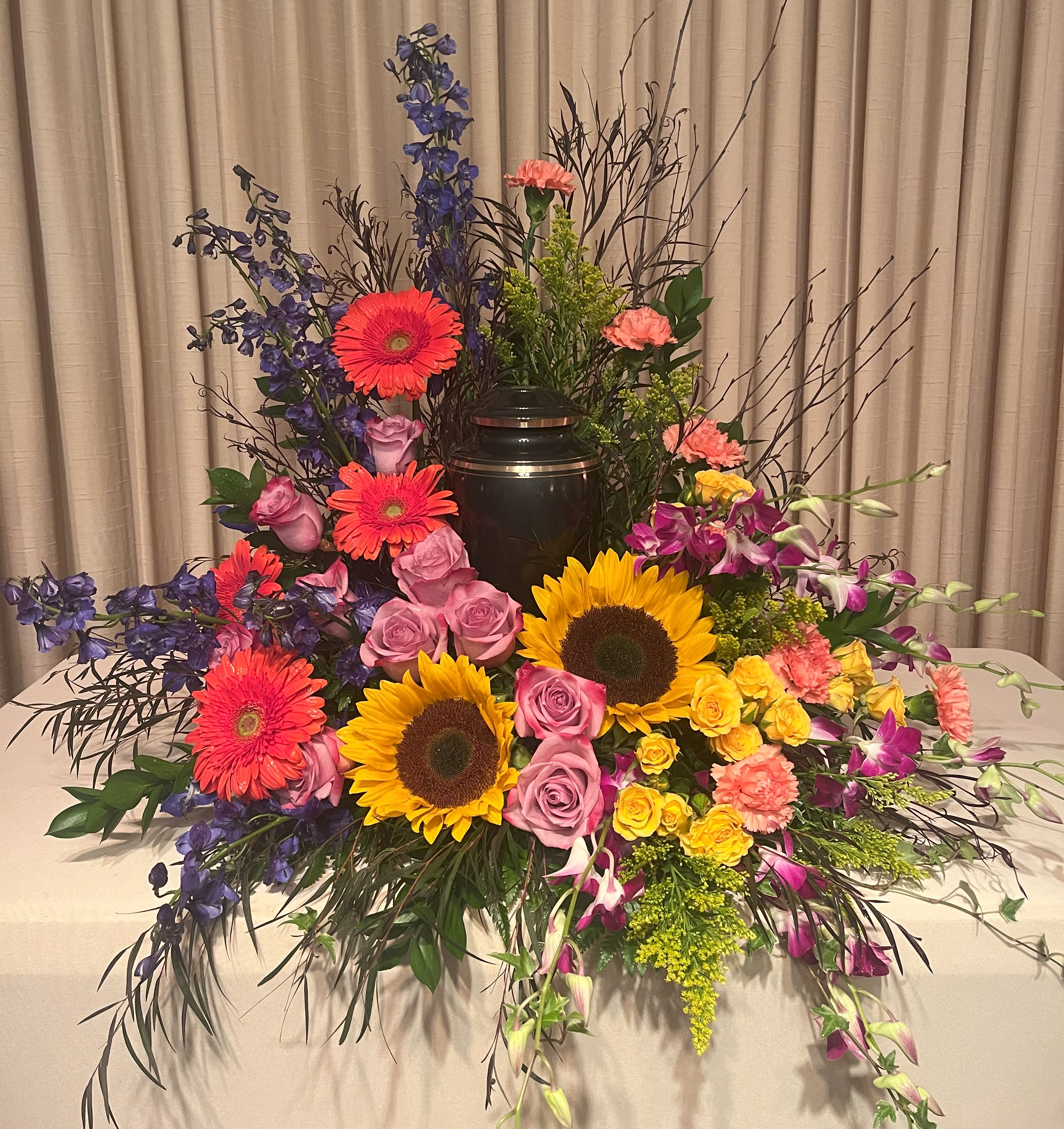 Large floral arrangement with sunflowers, roses, gerberas, and orchids around an urn