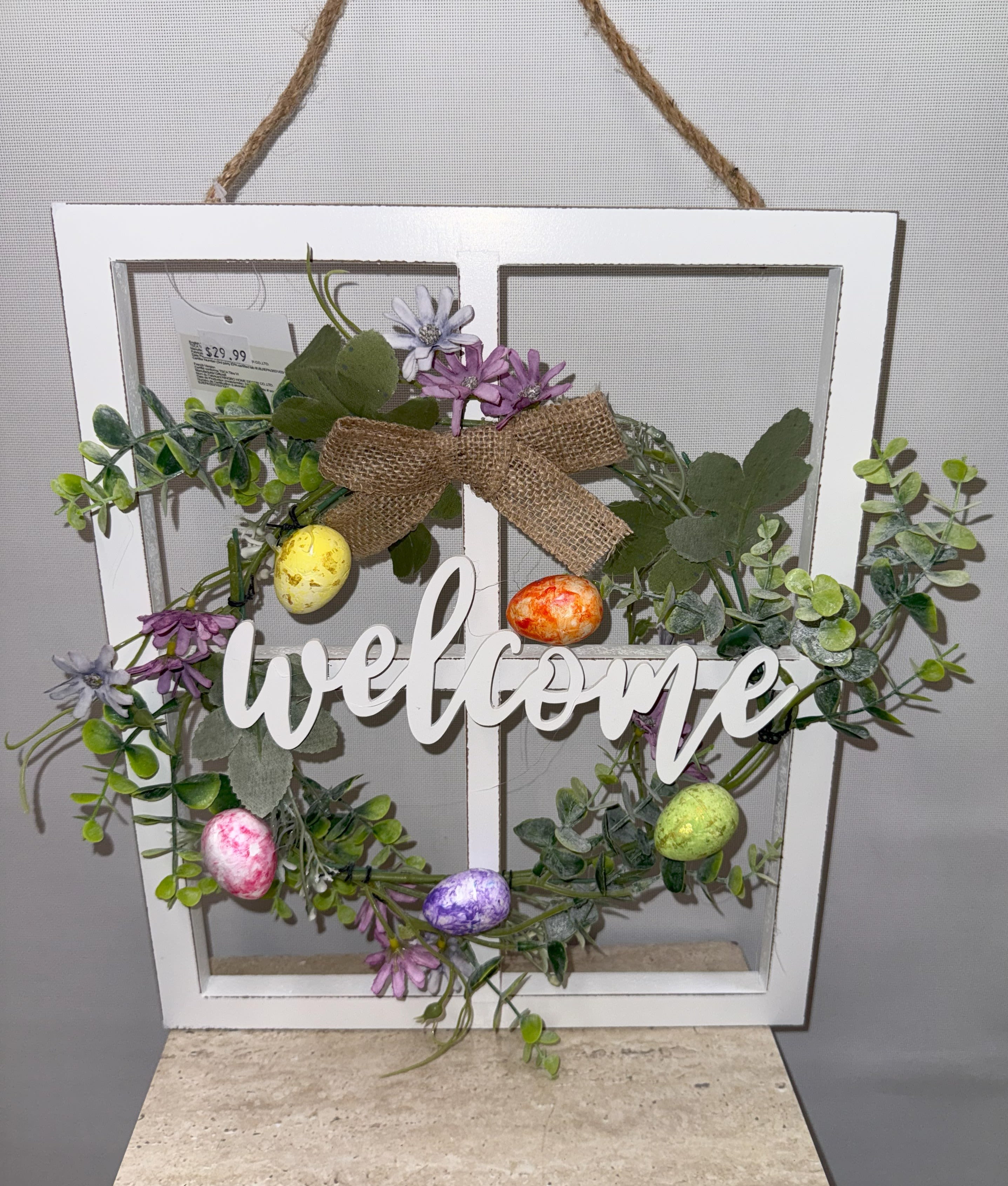 Decorative wreath in a white window frame with flowers, eggs, and a welcome sign