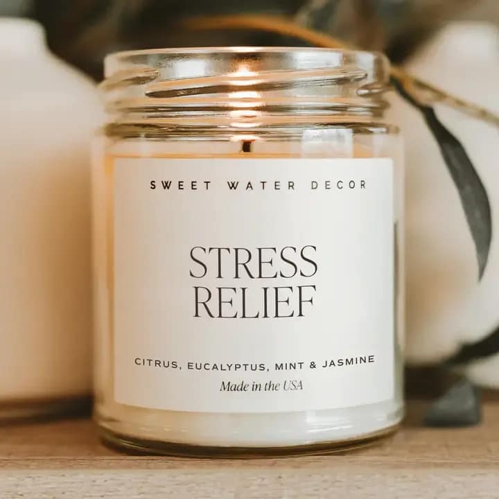 A glass jar candle labeled Stress Relief with a lit wick.