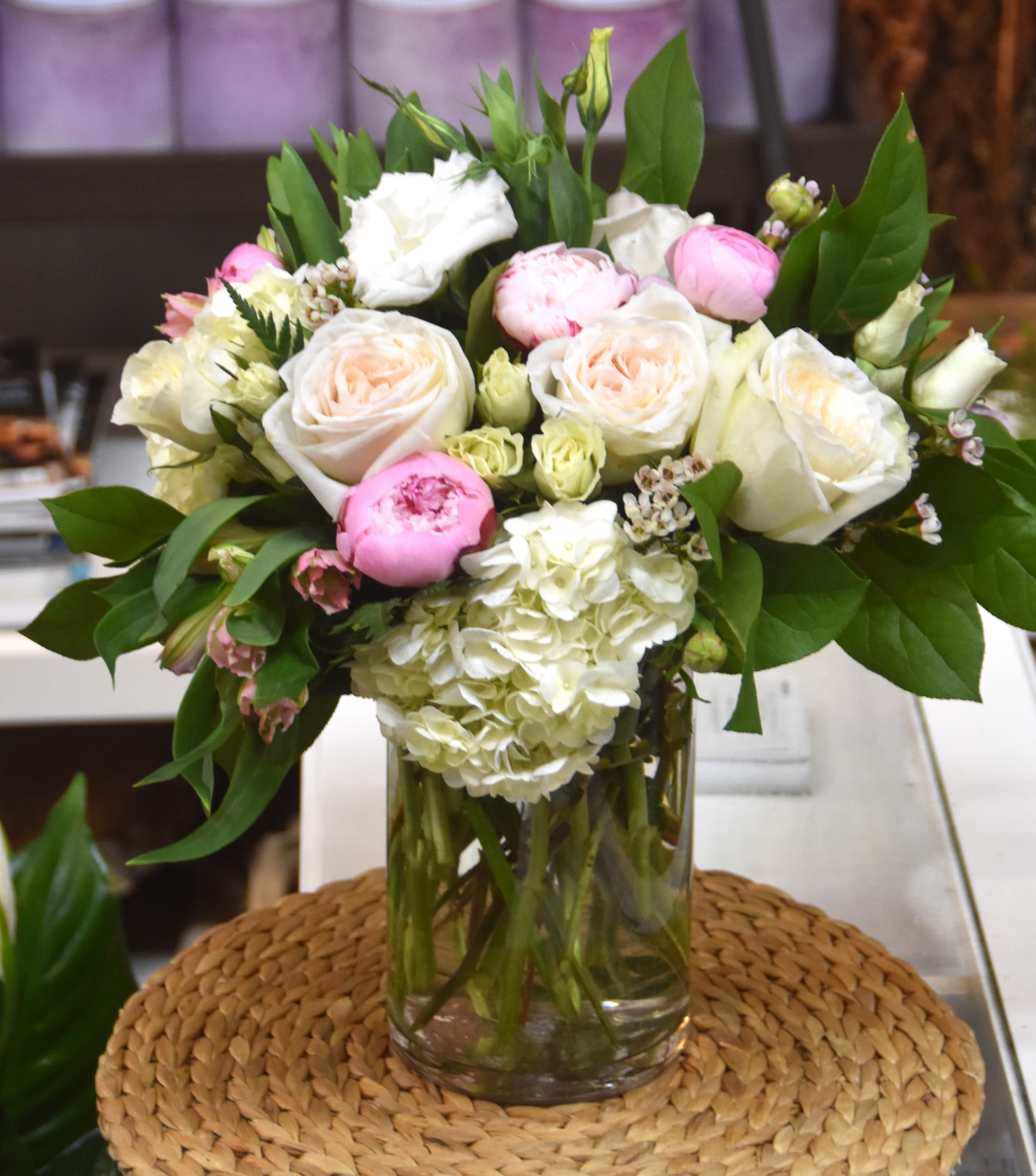 Glass vase arrangement with white hydrangeas, blush roses, and pink blooms with lush foliage