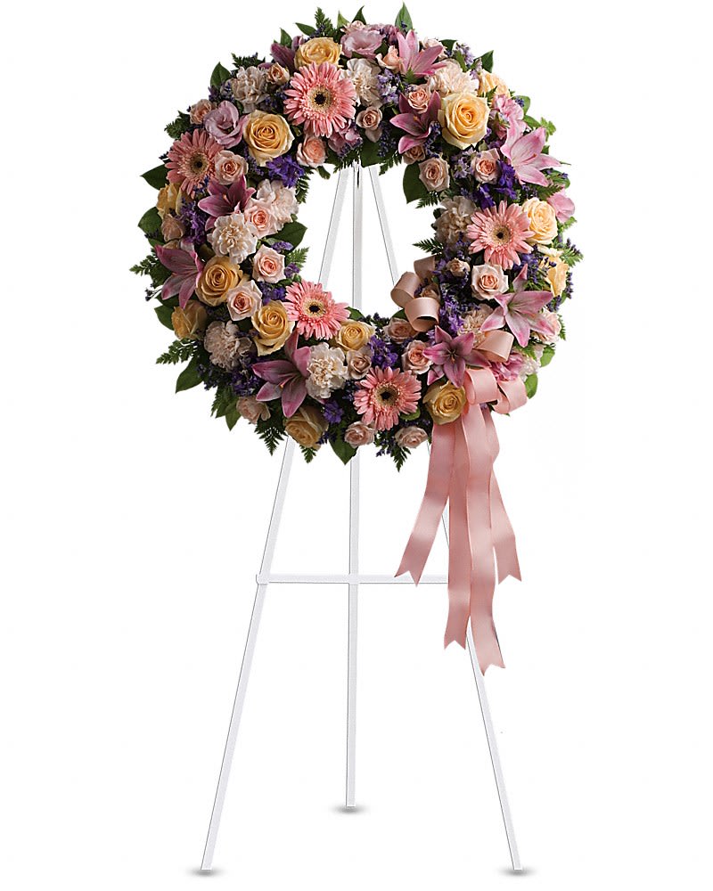 Floral wreath of pink, peach, and purple flowers on a white stand with ribbon