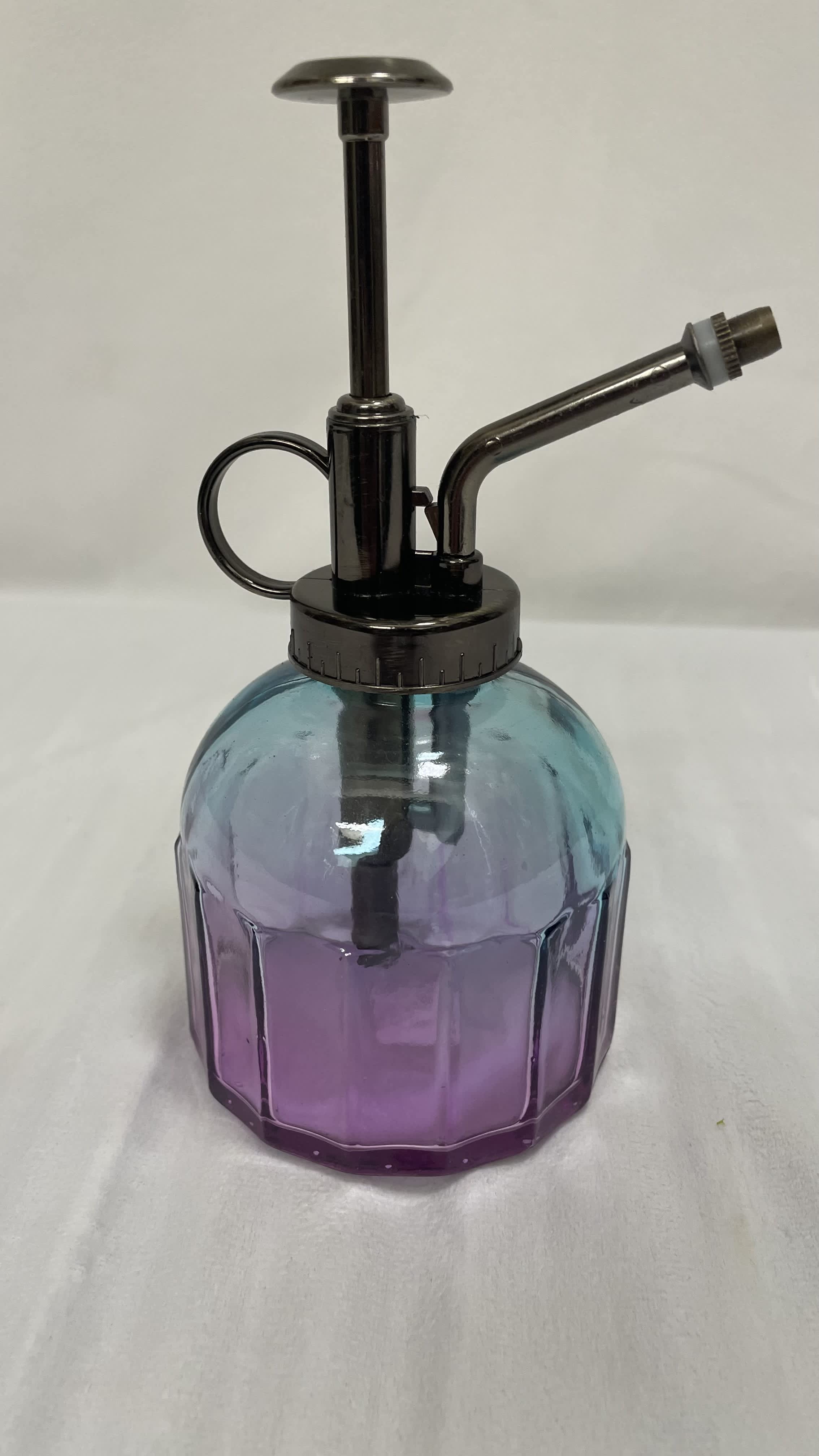 Small blue and purple glass plant mister with dark metal pump and nozzle on a light surface