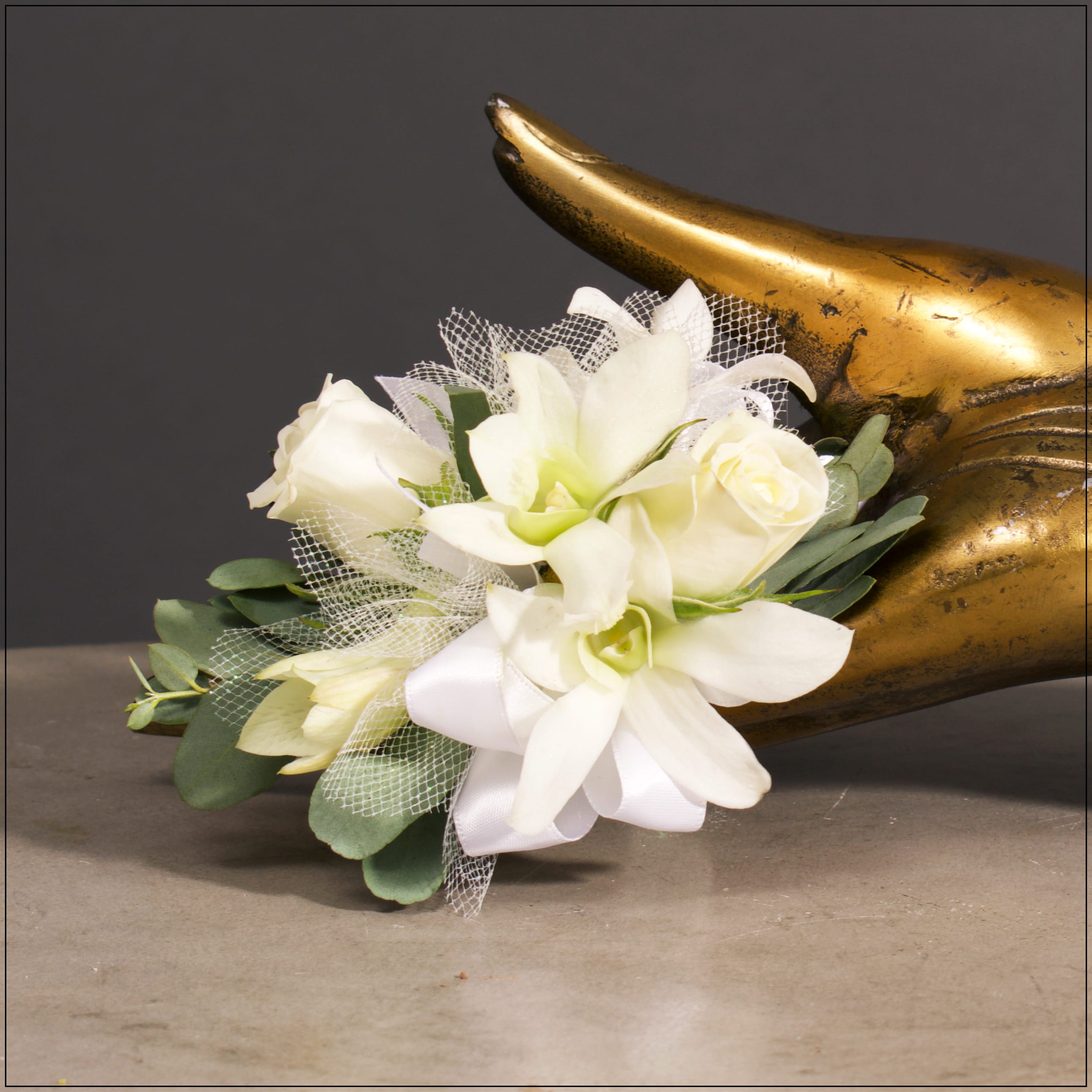 White floral corsage with roses and orchids beside a gold horn